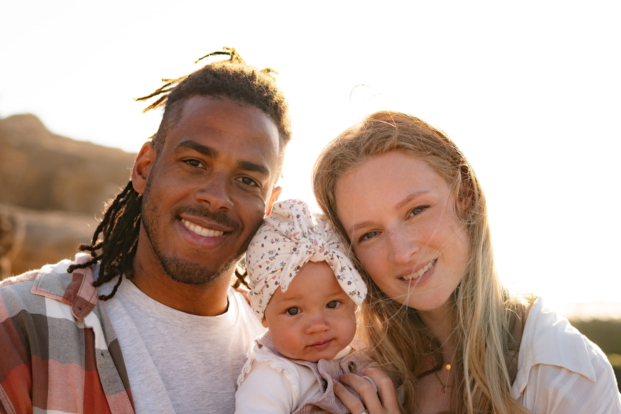 Close portrait of father, mother and baby girl smiling in warm sunset light