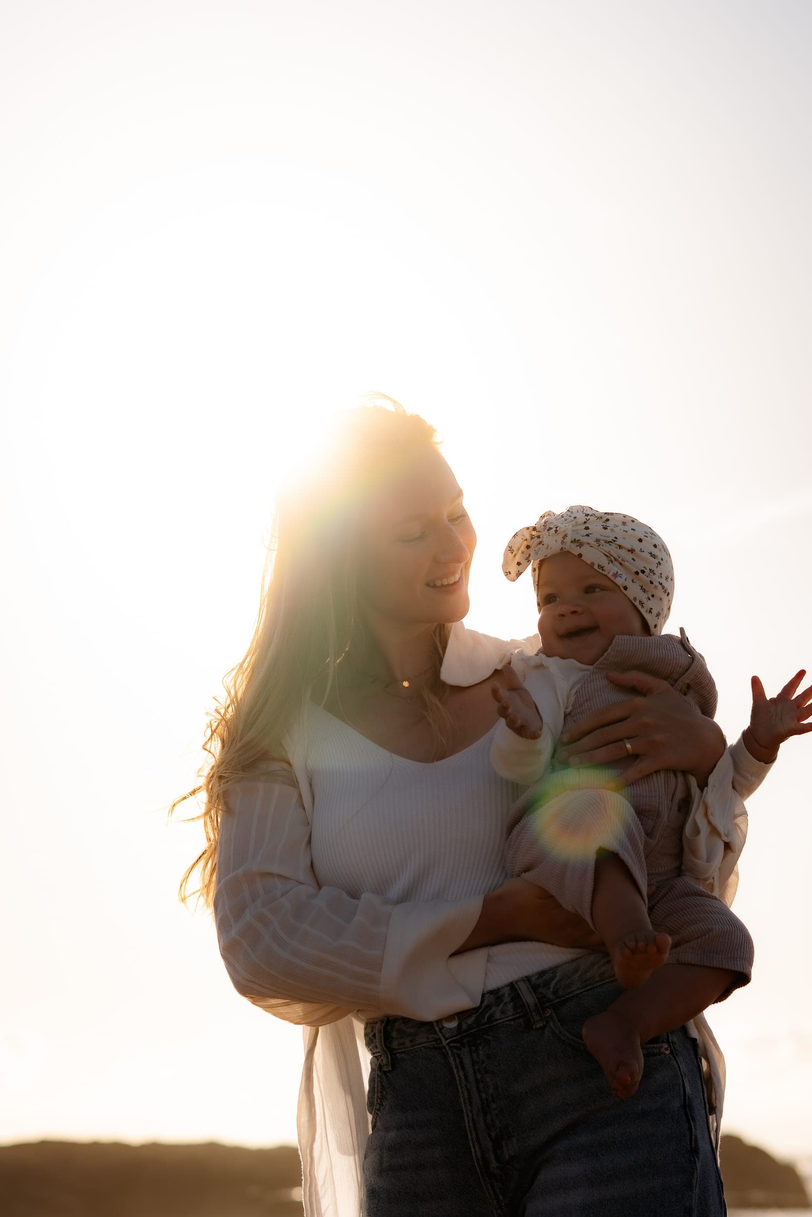 Mother holding smiling baby in sun flare light on the beach at golden hour