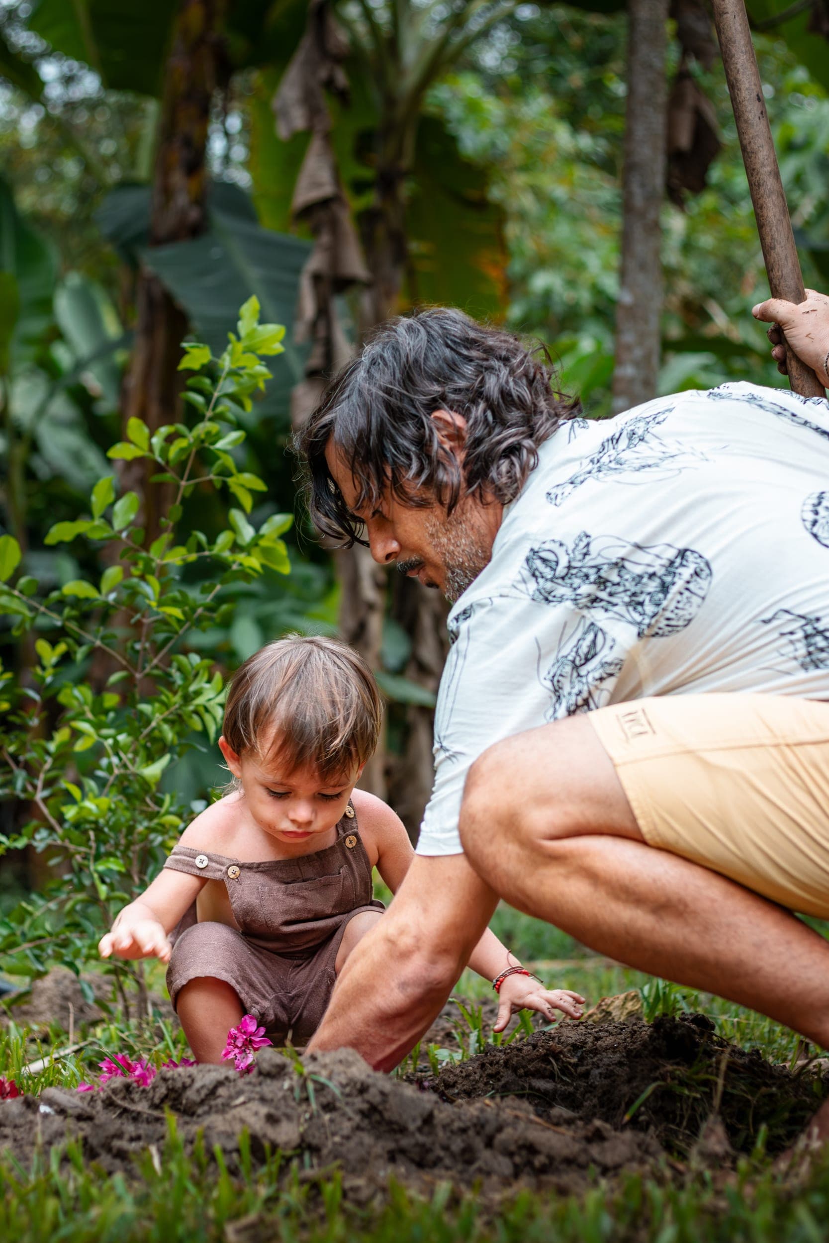 Father and toddler crouching to plant flowers in dark soil in a tropical garden
