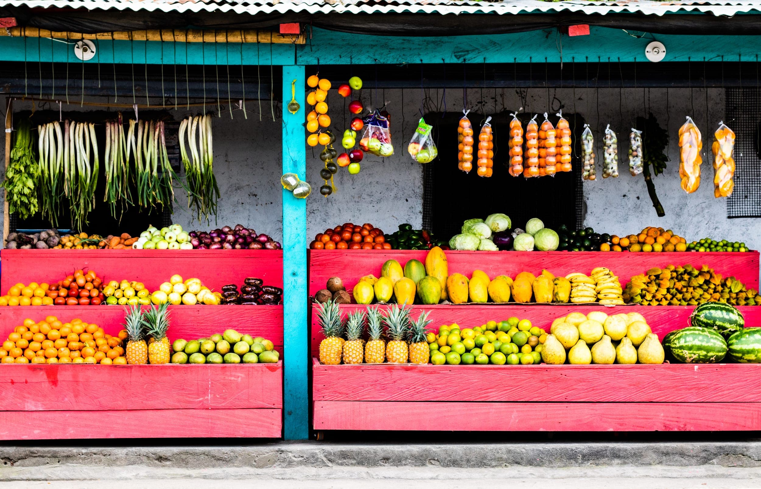 Colourful roadside fruit and vegetable stand with pineapples, papayas and hanging produce