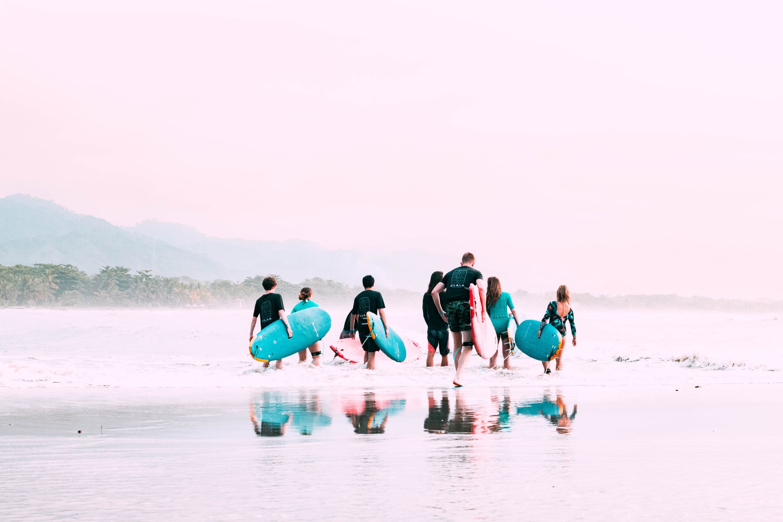 Group of surfers walking into the sea with colorful boards at a soft pink dawn