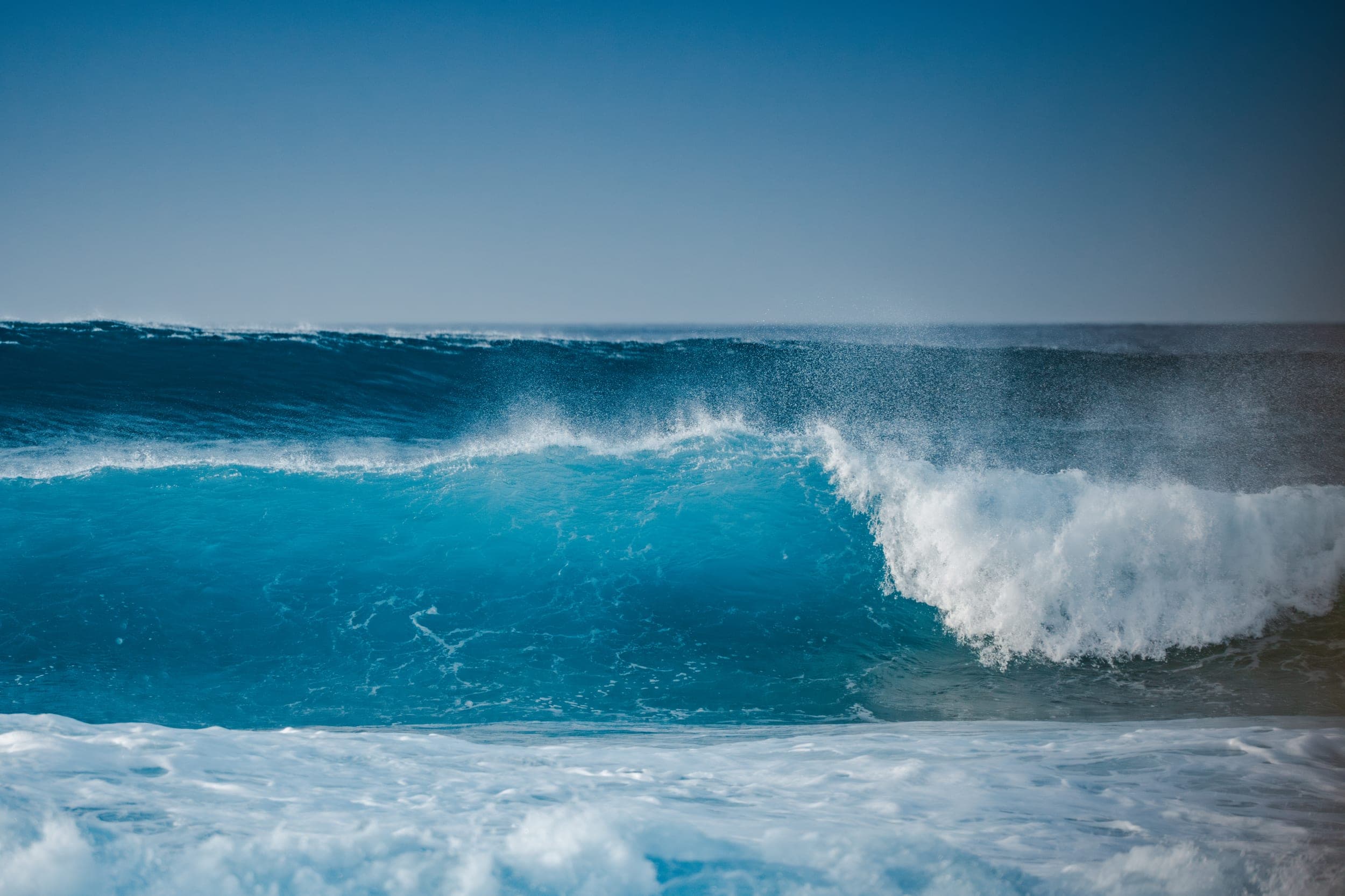 Turquoise wave curling and breaking into white foam under a clear blue sky