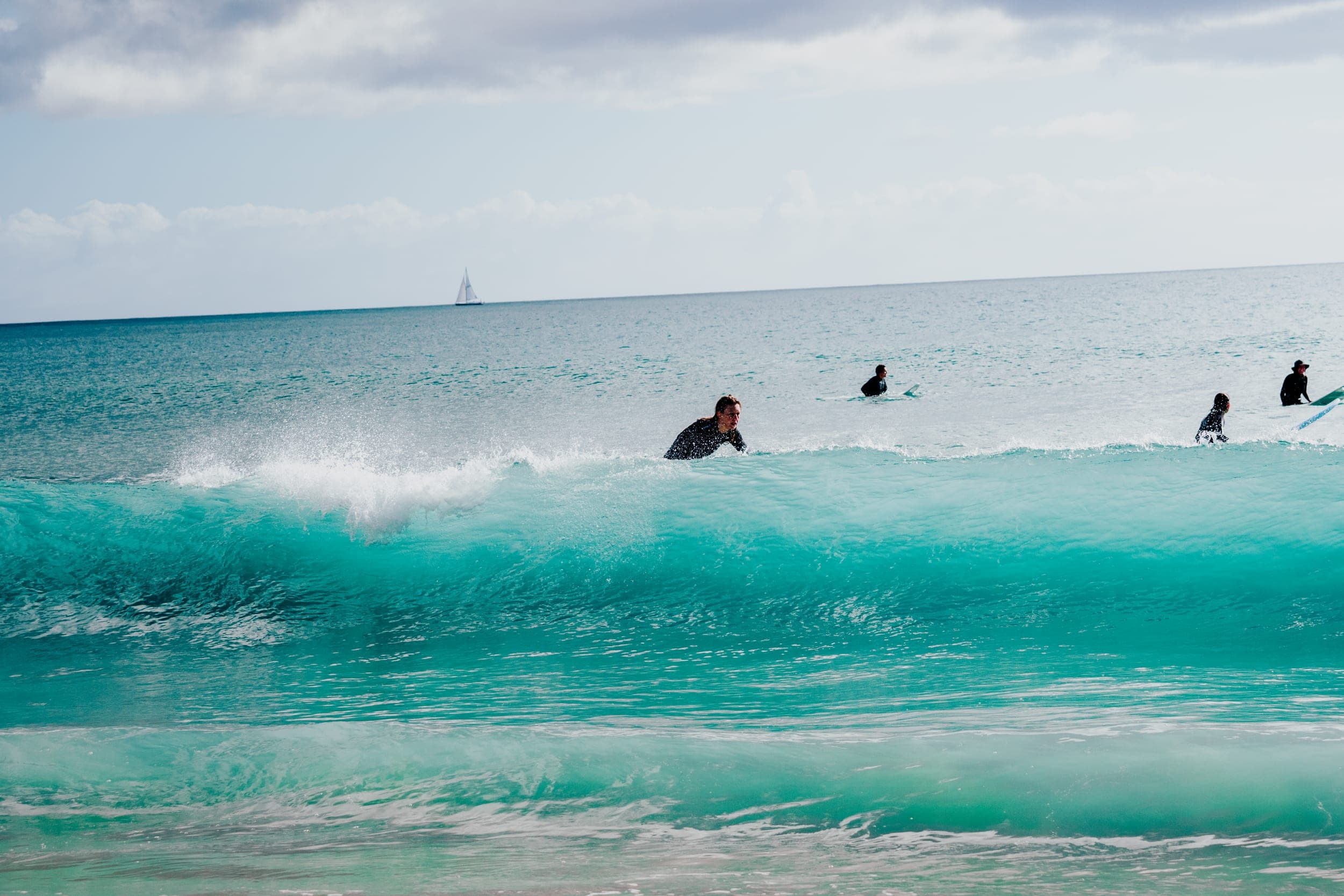 Surfer in a wetsuit riding the face of a turquoise wave with others waiting behind
