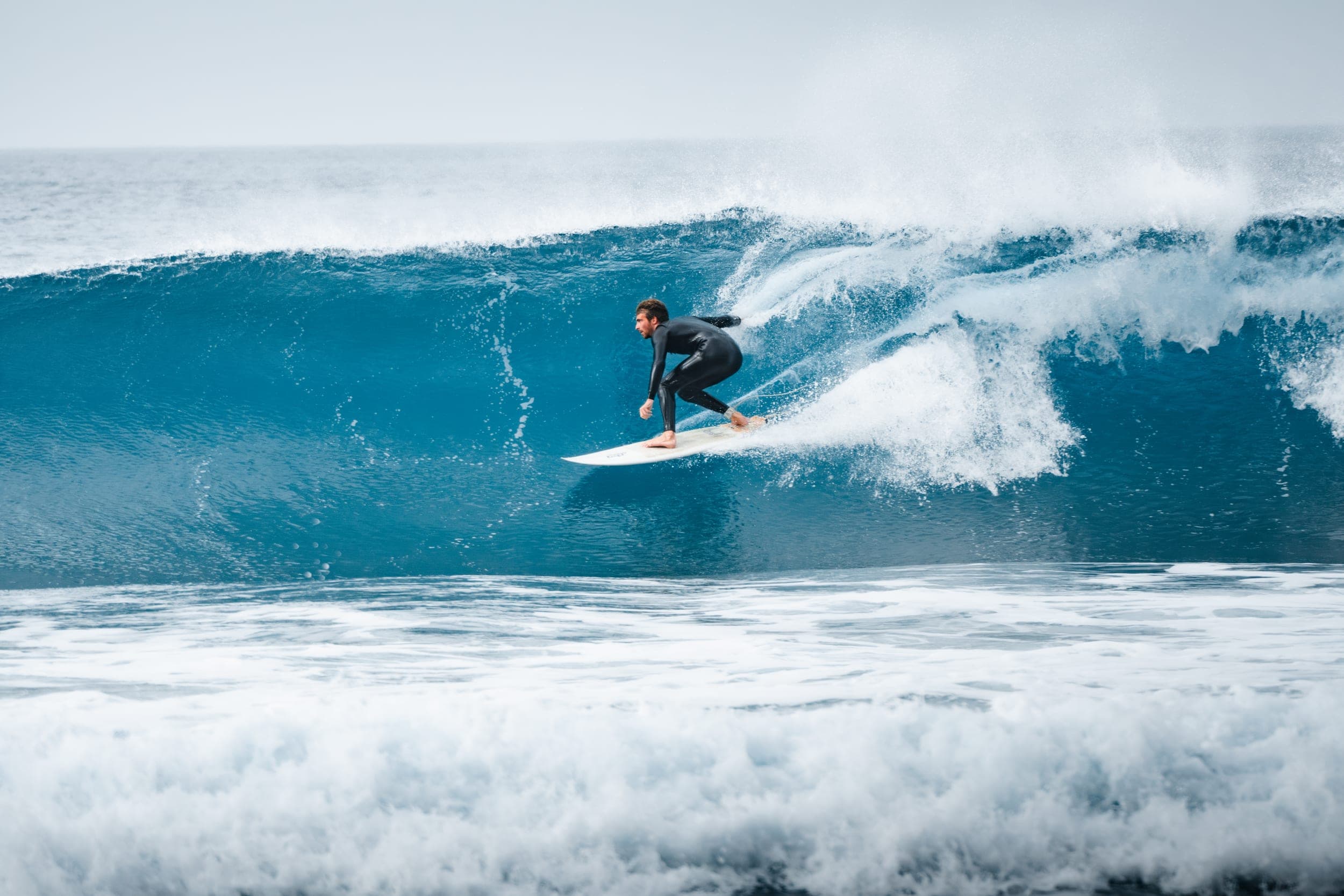 Surfer in a black wetsuit carving down the face of a big blue wave
