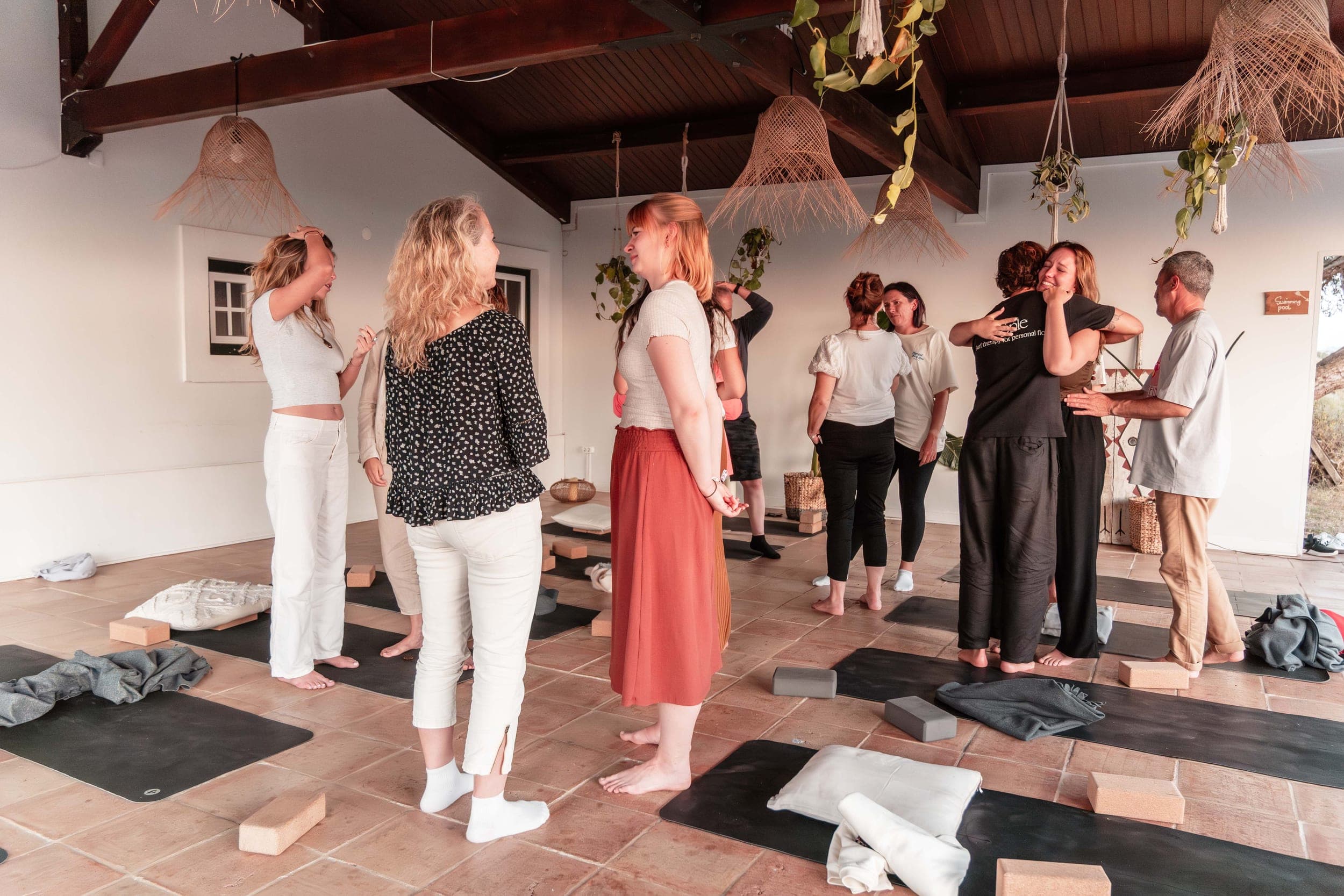 Retreat group embracing and connecting on yoga mats in a bright plant-filled studio