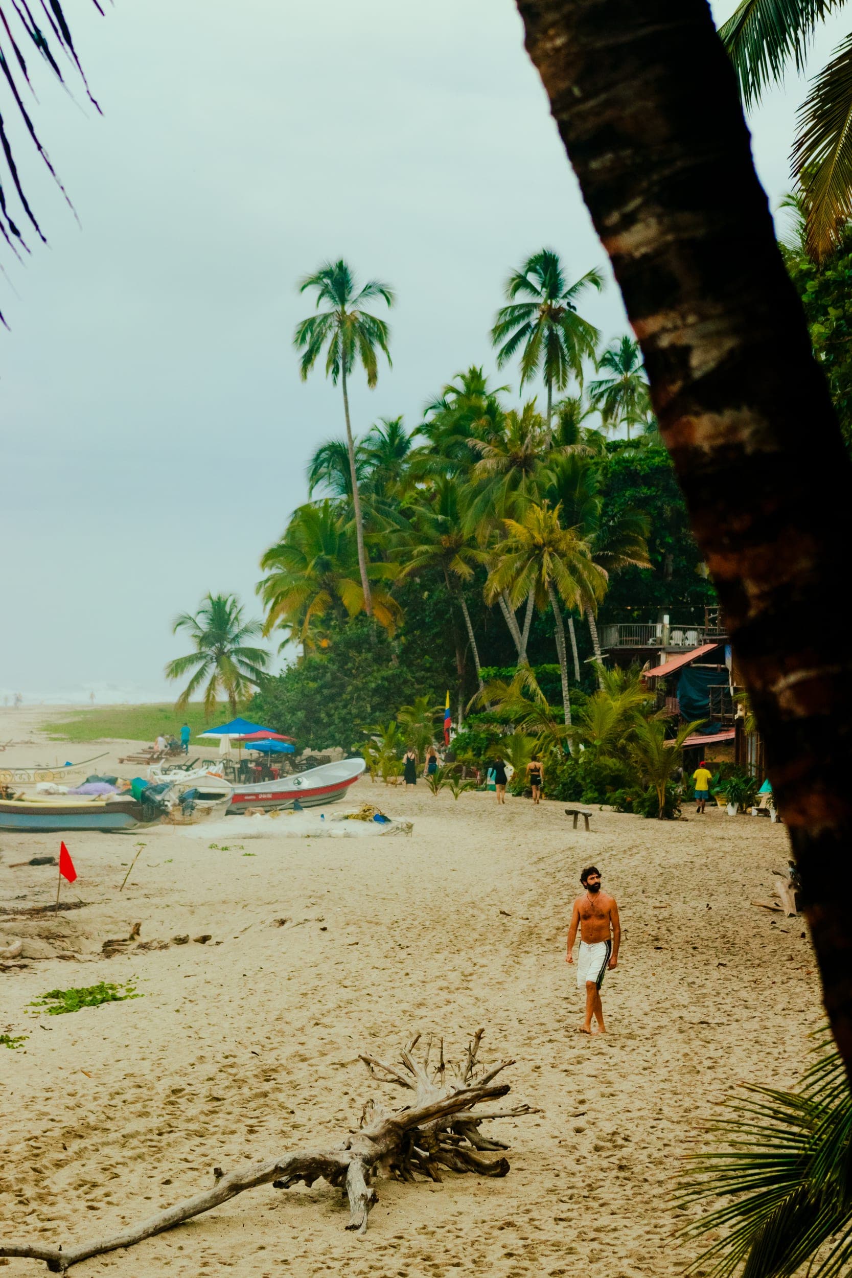 Shirtless man walking on a palm-fringed tropical beach with fishing boats