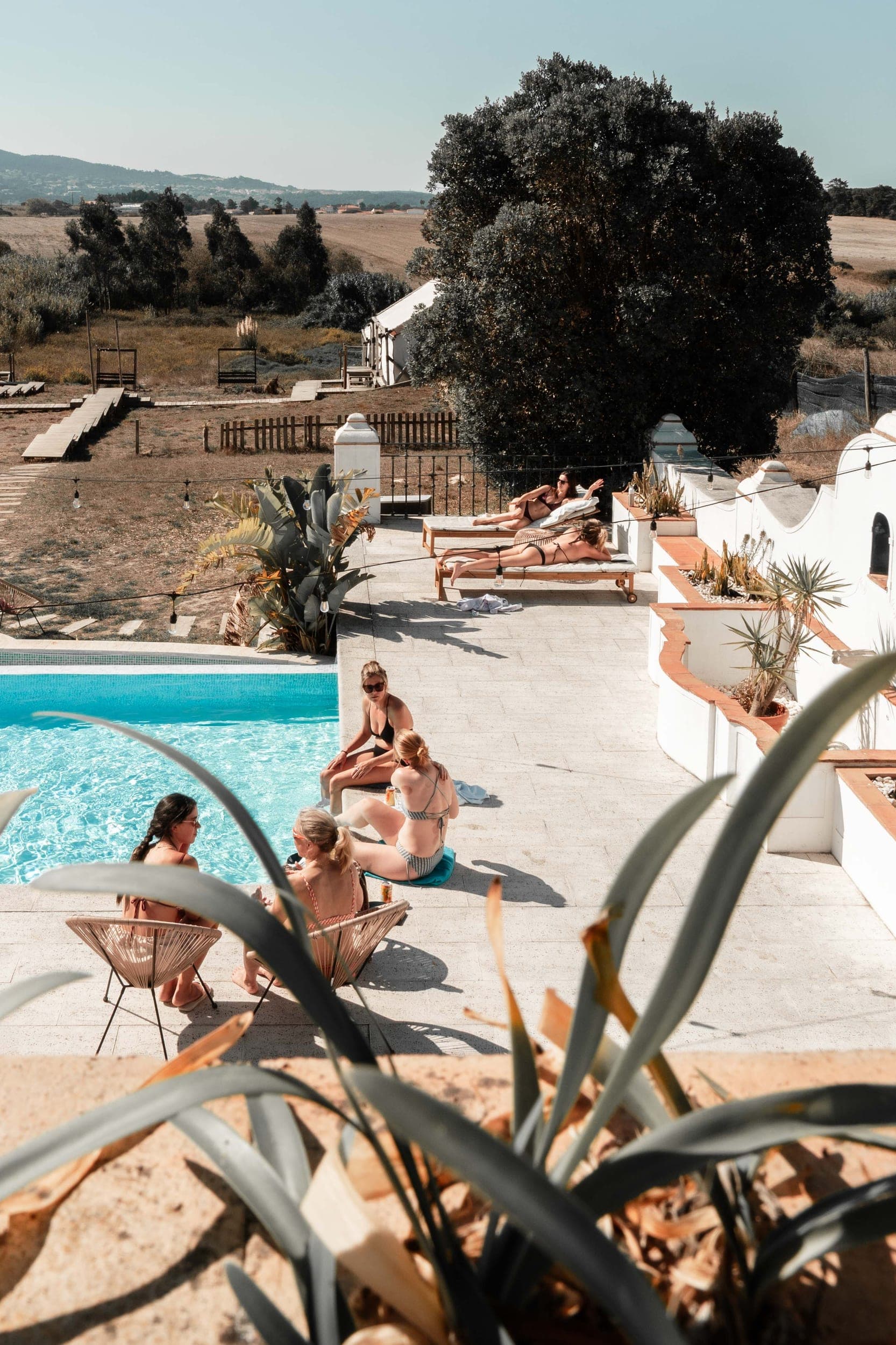 Women in swimwear relaxing and sunbathing around a pool overlooking countryside