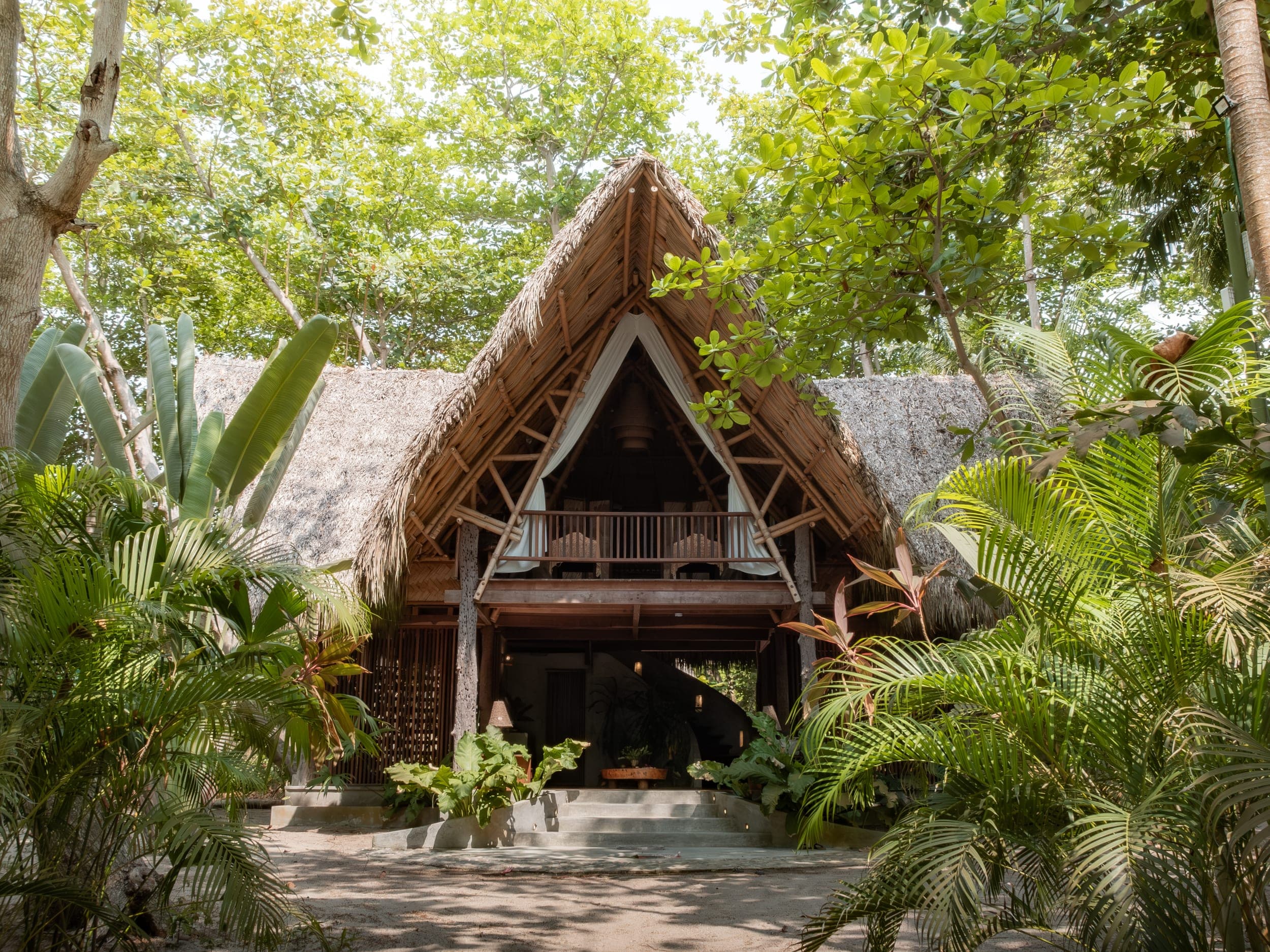 Thatched-roof A-frame retreat lodge surrounded by lush tropical greenery