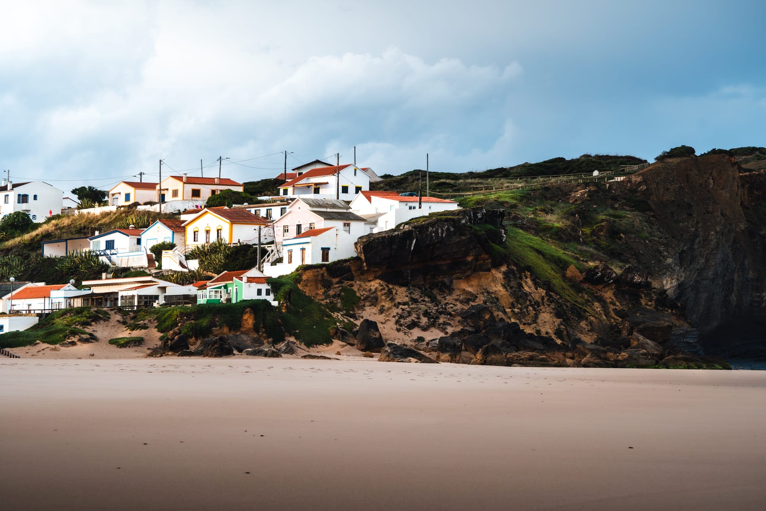 Colorful Portuguese coastal village houses on a cliff above an empty sandy beach