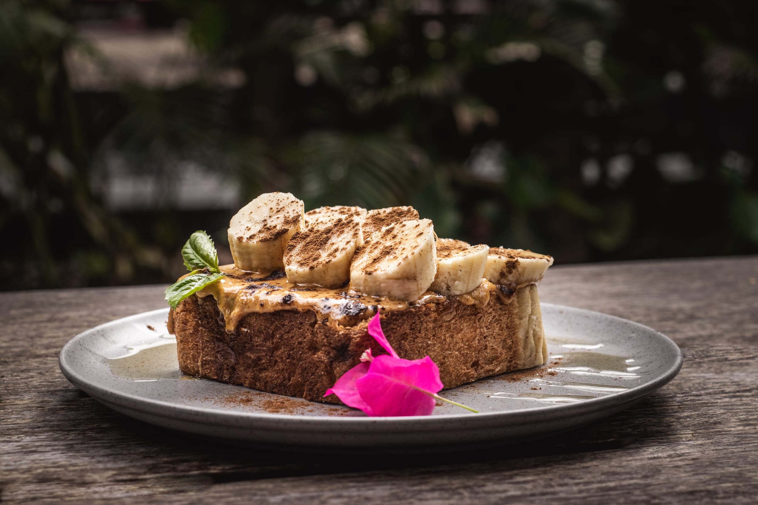 Banana and peanut butter toast dusted with cinnamon on a plate in a garden