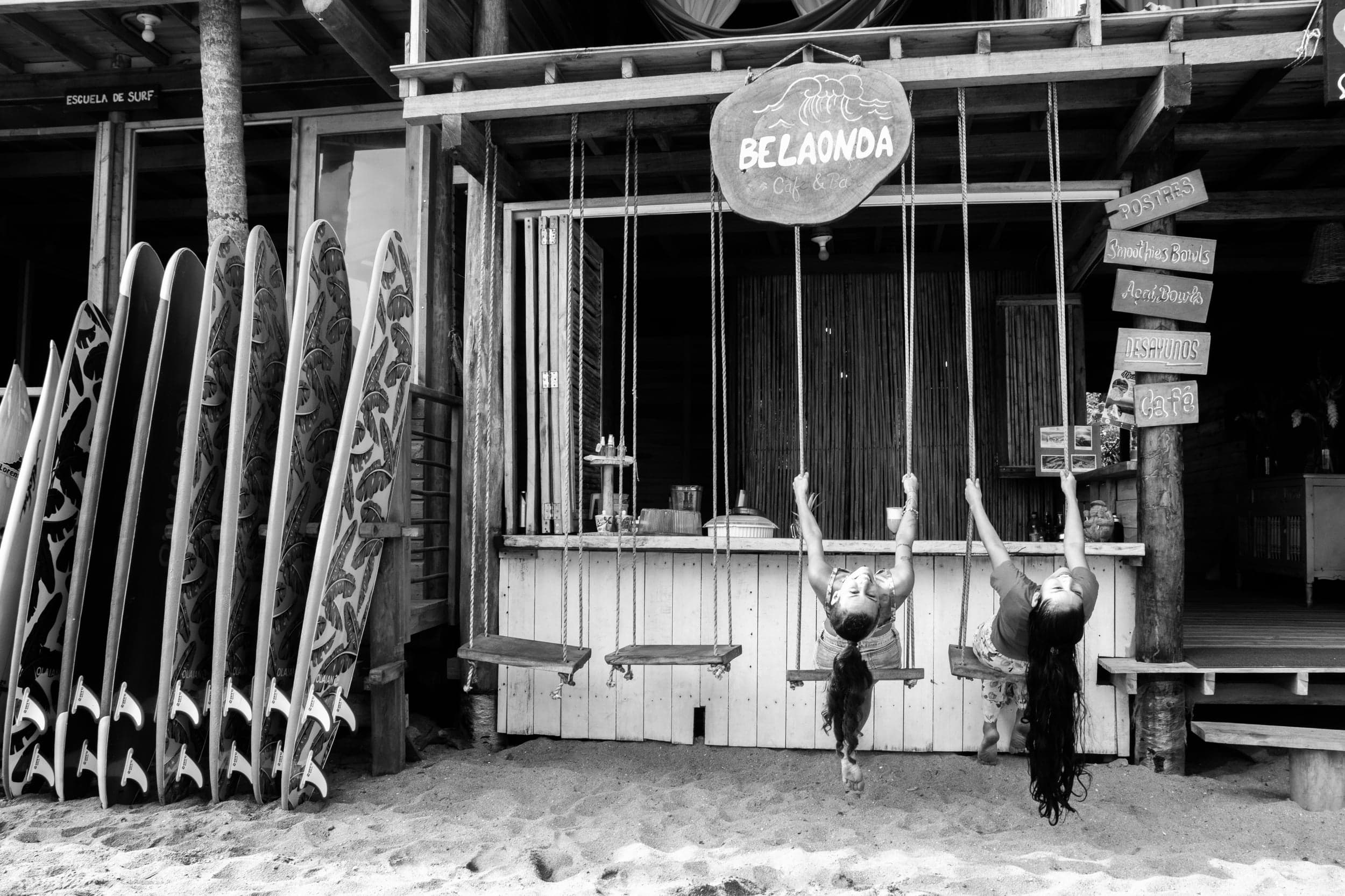 Black-and-white shot of two girls on rope swings outside a beach surf cafe