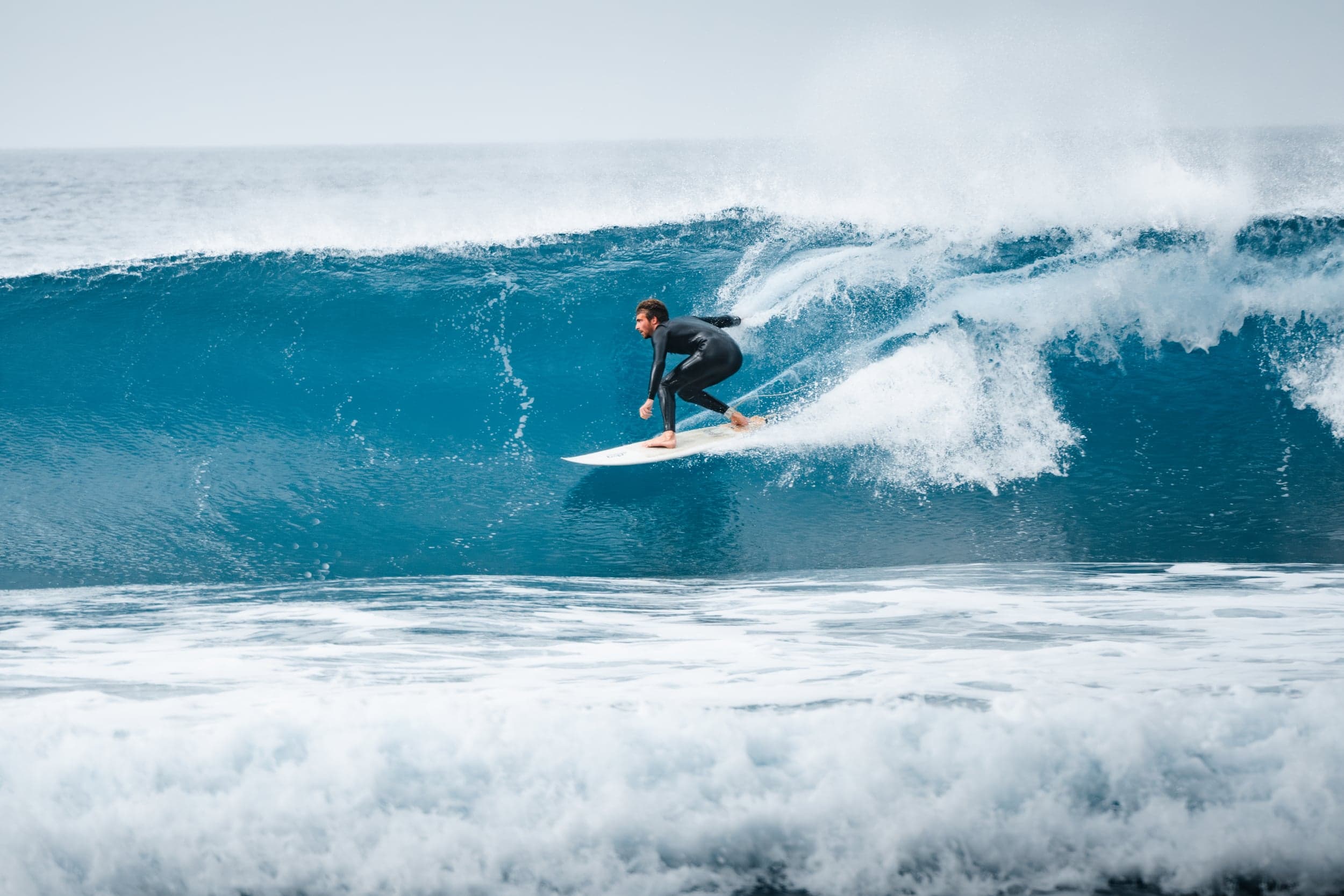 Surfer crouched low racing across a glassy blue wall of water
