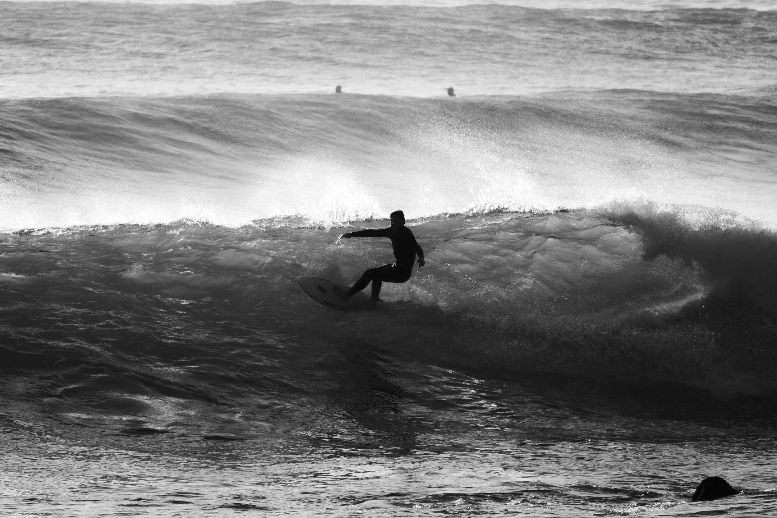 Black-and-white silhouette of a surfer carving down the face of a wave