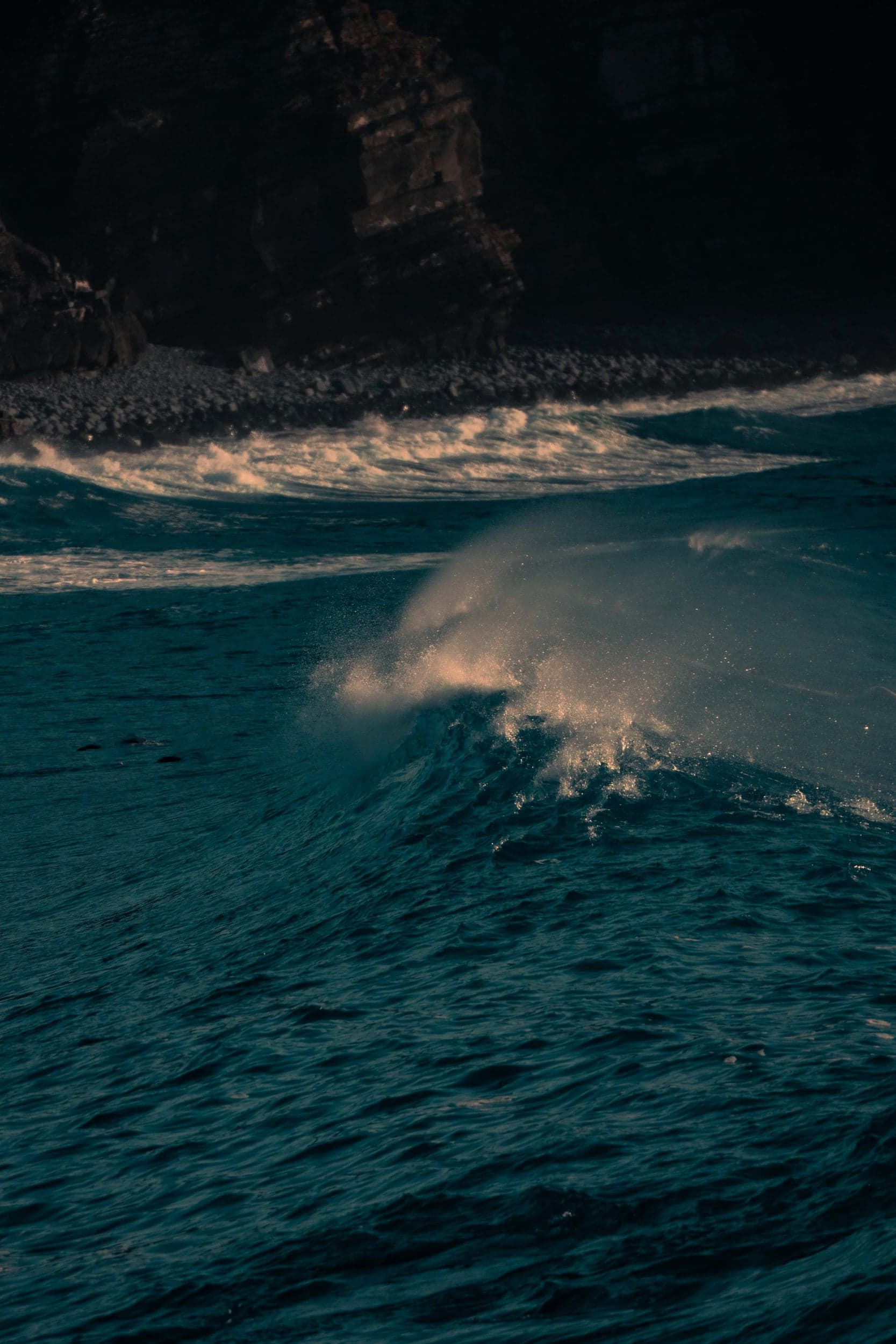 Wave breaking off dark rocks with backlit spray catching golden light