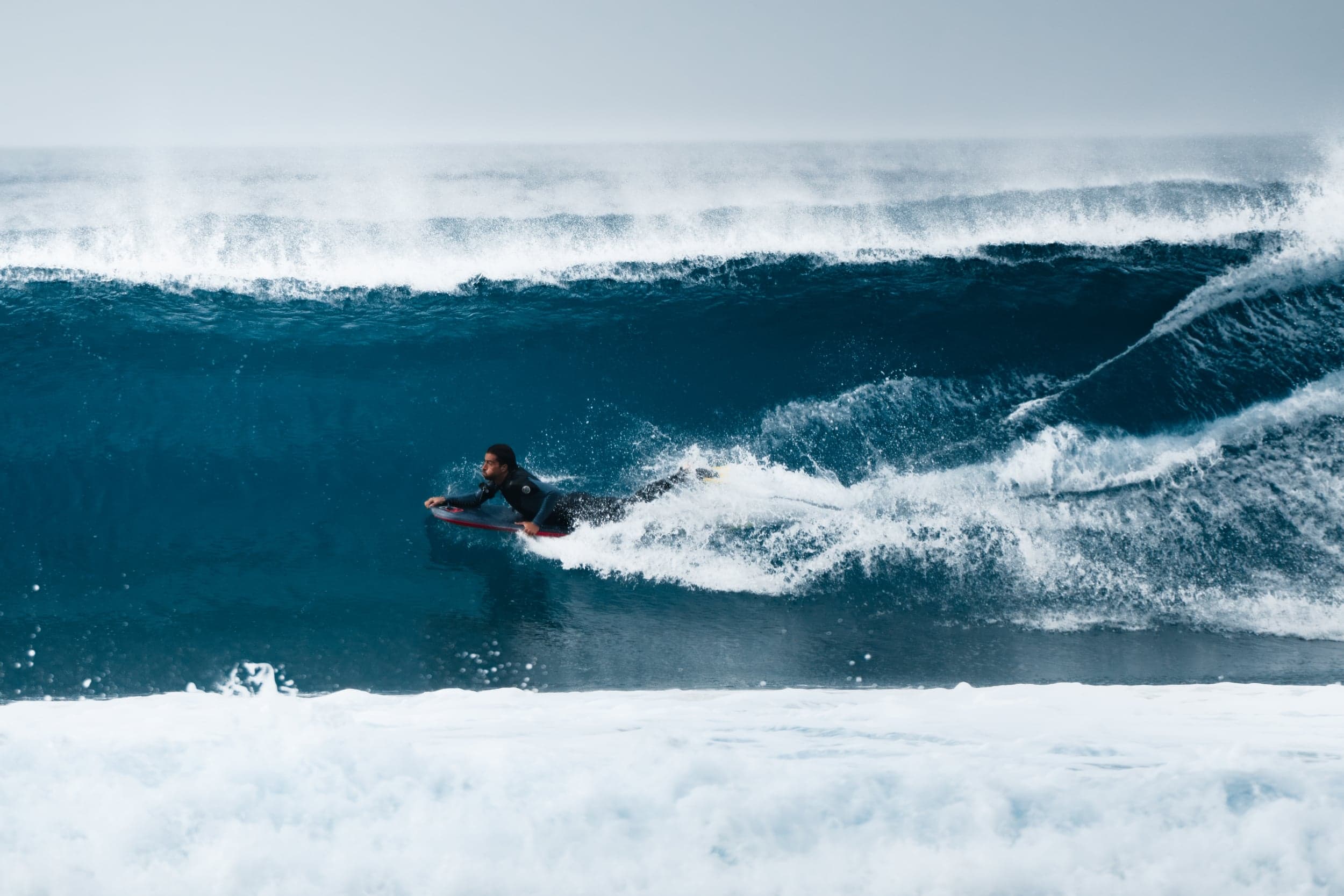 Surfer laying into a bottom turn under the lip of a big blue wave