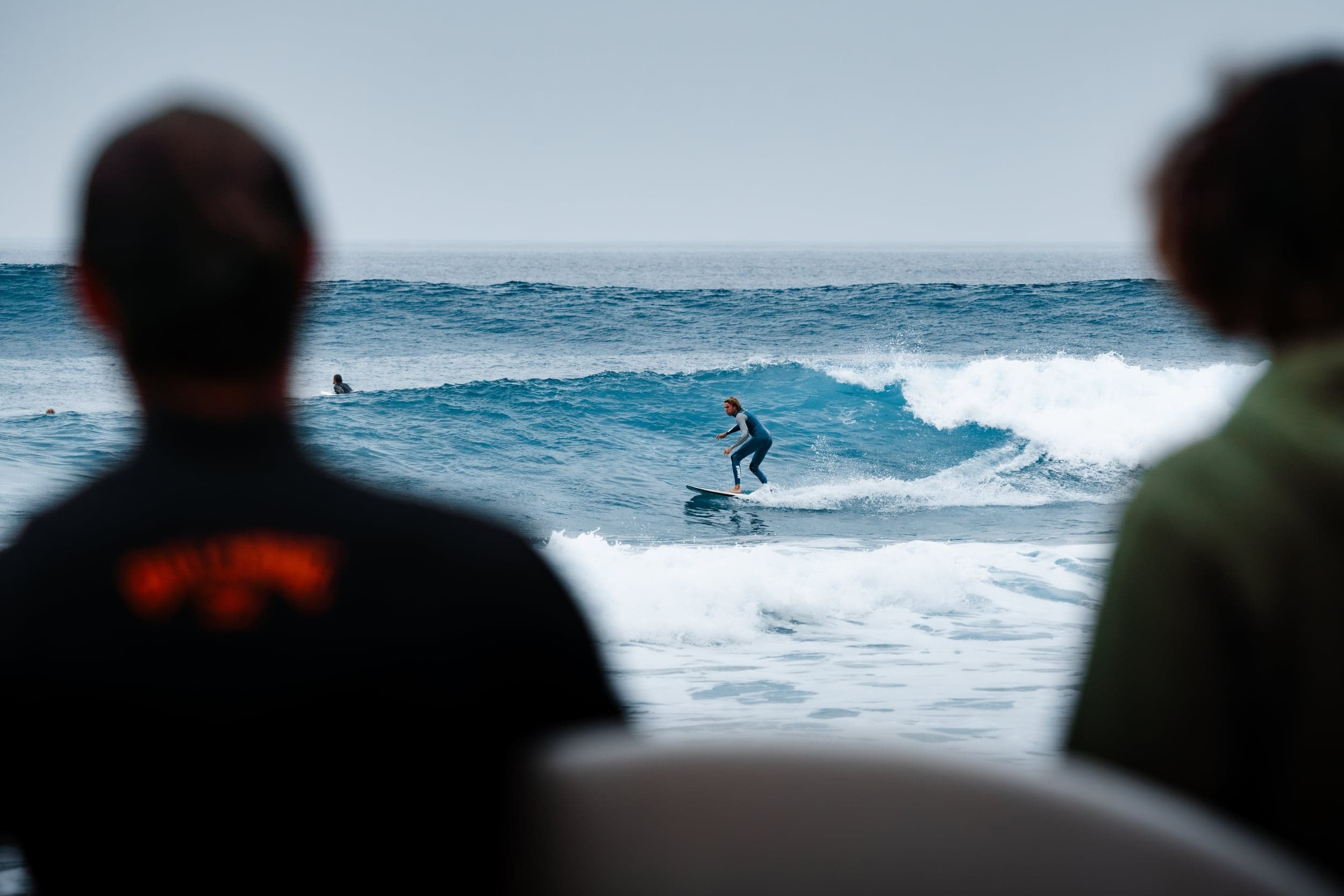 Surfer riding a wave framed between two blurred spectators watching from shore