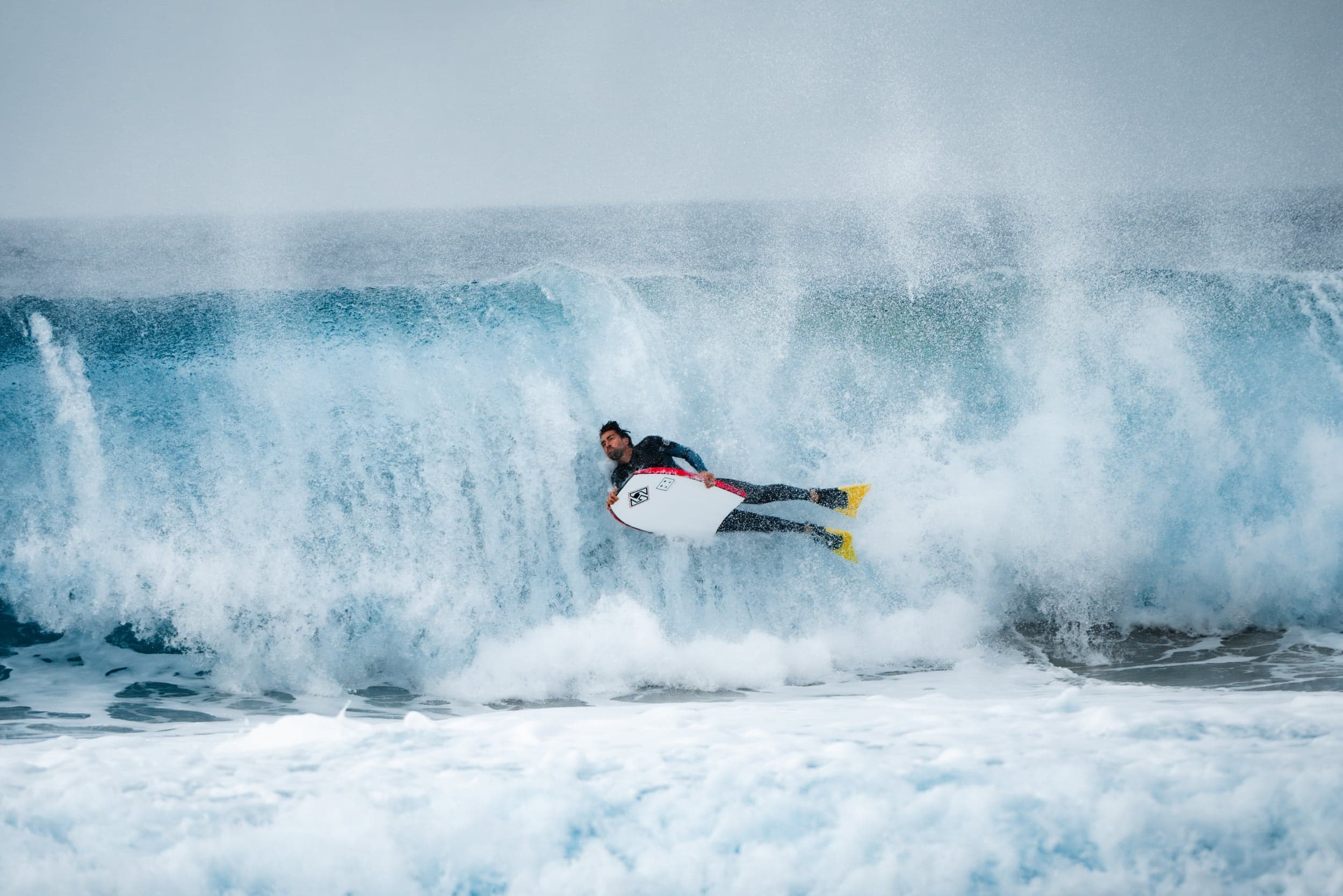 Bodyboarder wiping out mid-air off a big wave, yellow fins flying