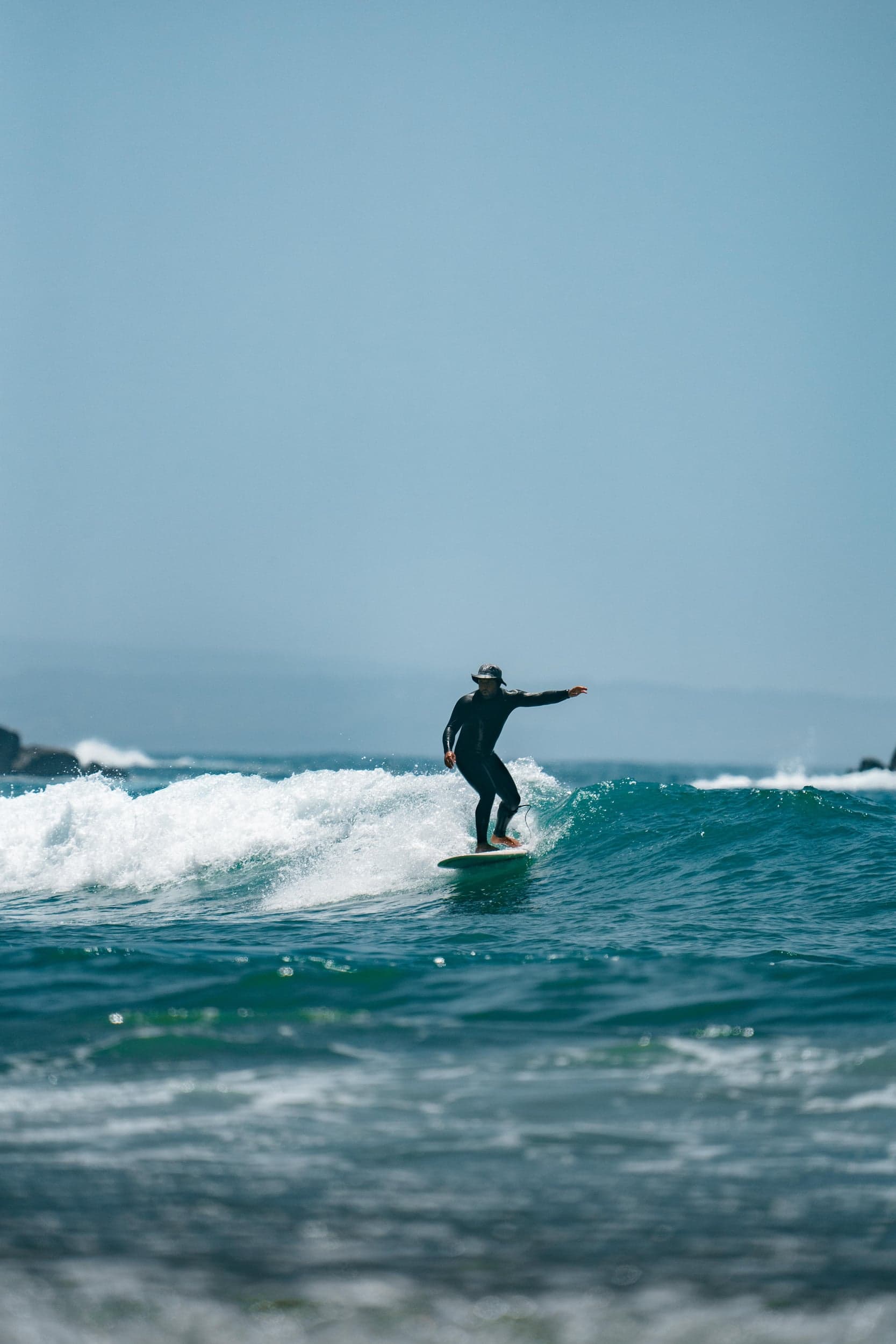 Surfer in a bucket hat riding a small clean wave under a bright blue sky