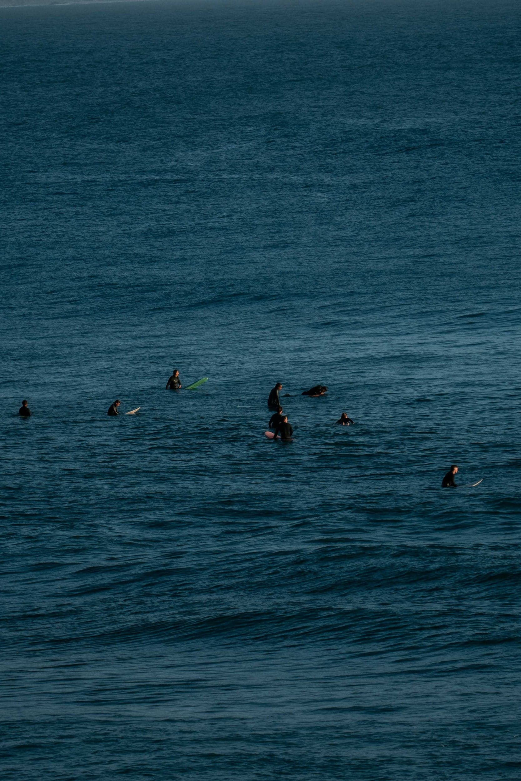 High-angle view of a scattered lineup of surfers waiting on deep blue water