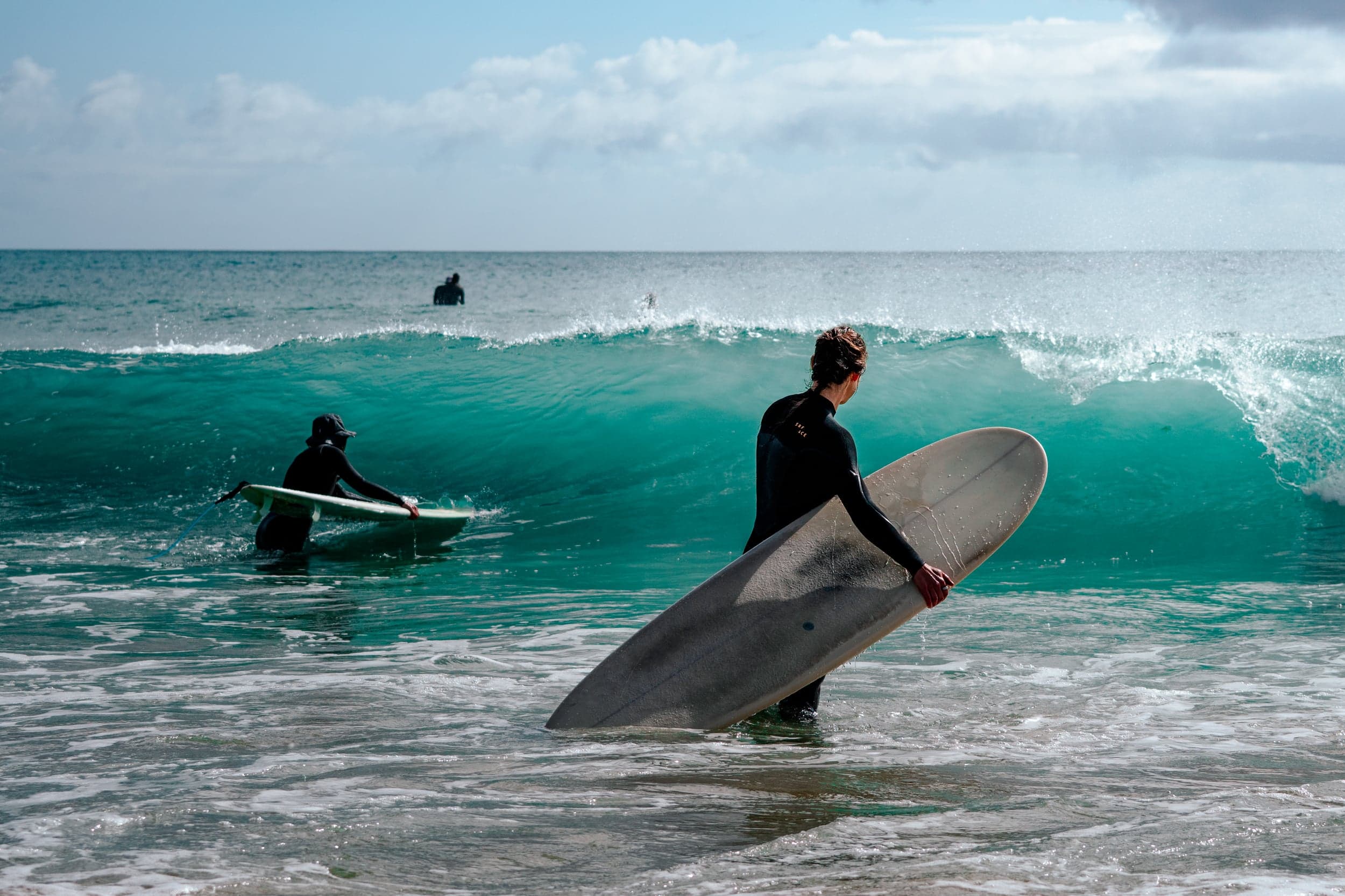 Two surfers wading out through clear turquoise shorebreak