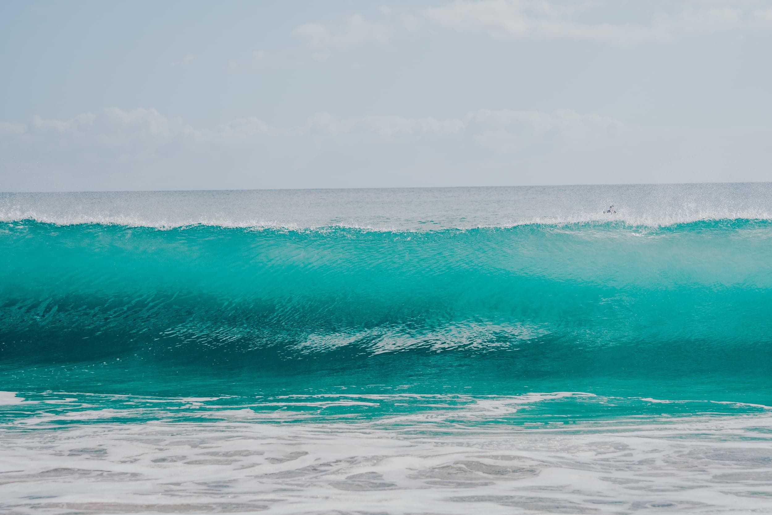 Empty turquoise wave curling toward shore under a hazy sky