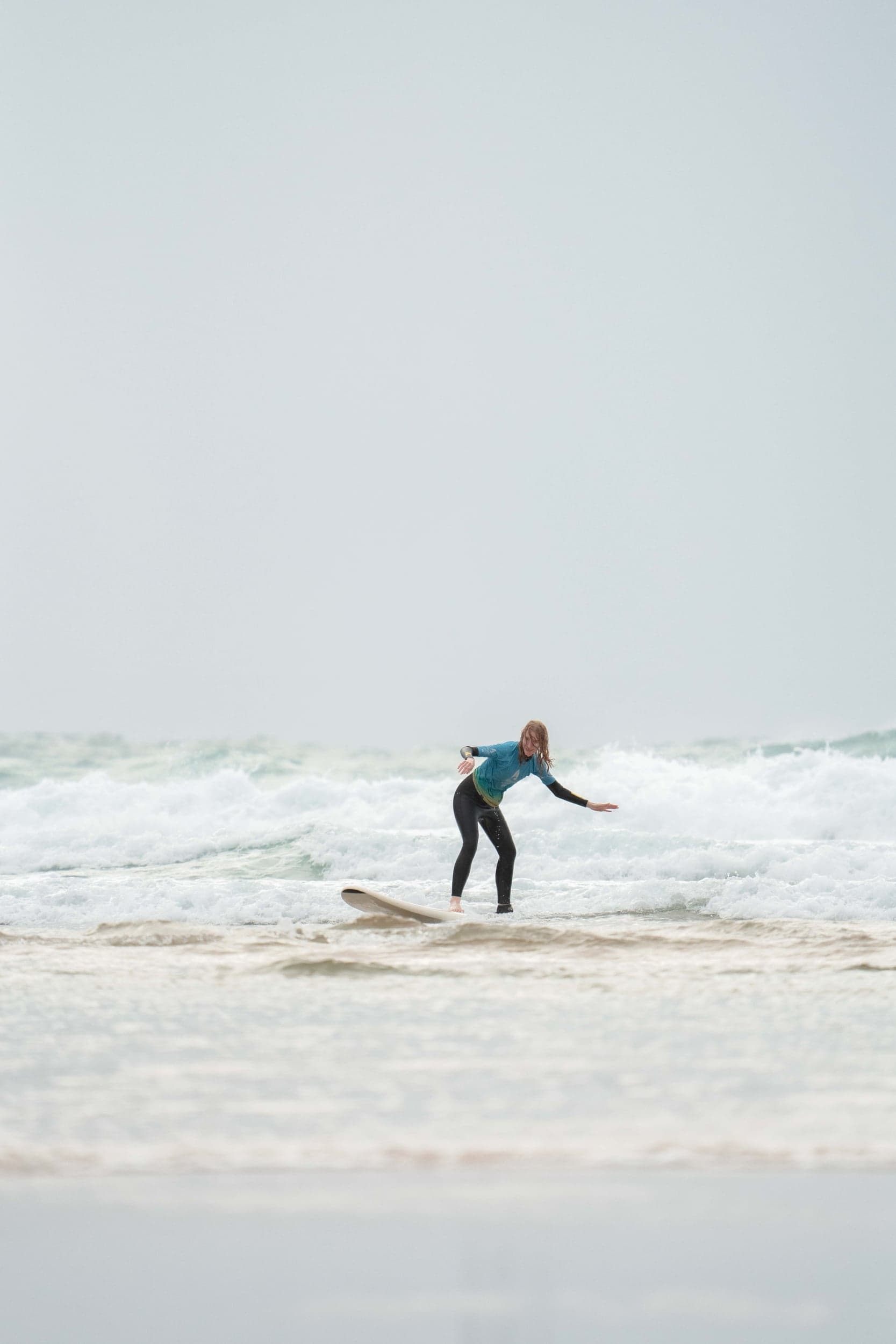 Woman in a blue rash vest riding a foamboard through whitewater on a grey day