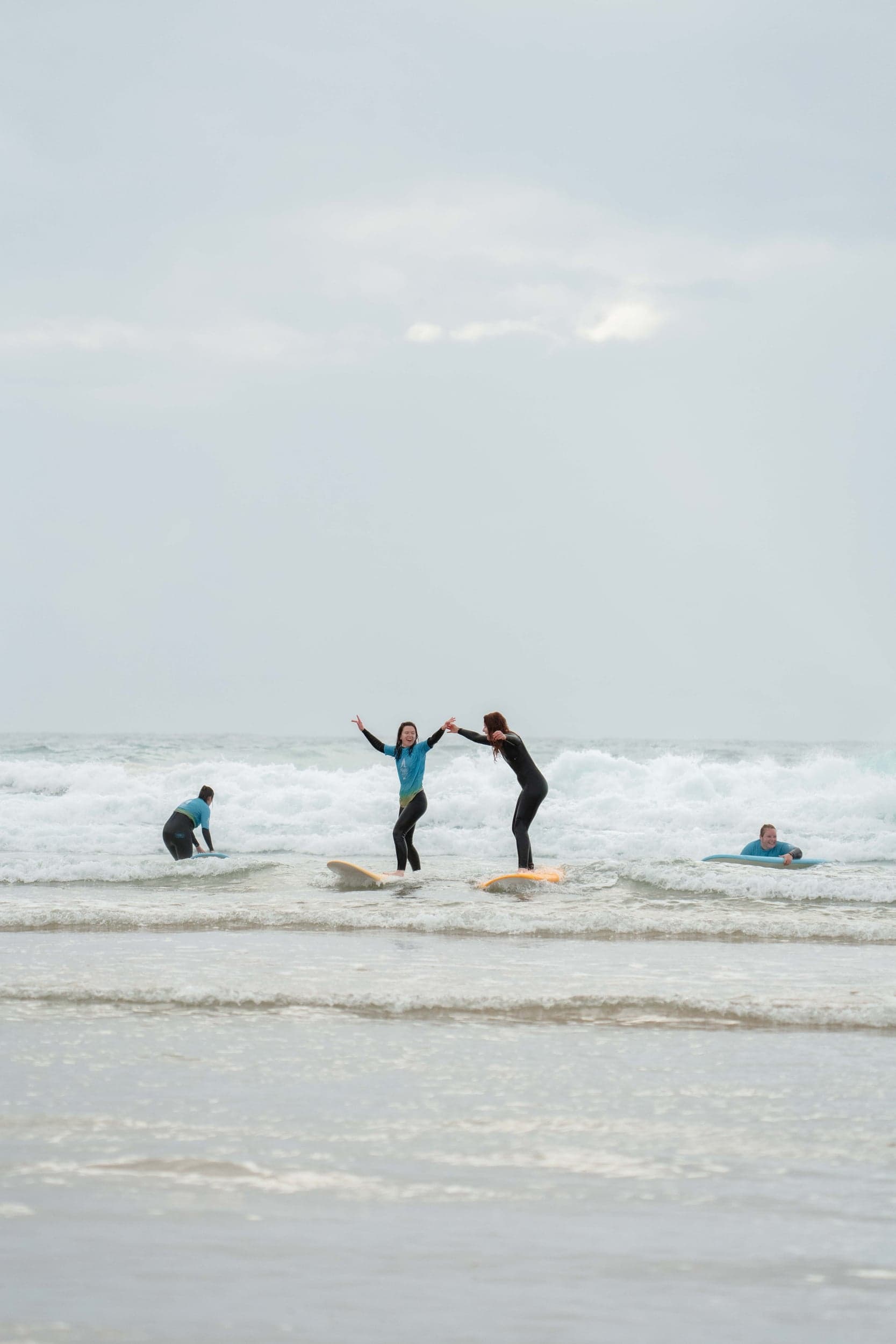 Two women laughing and high-fiving on surfboards in the whitewash during a lesson