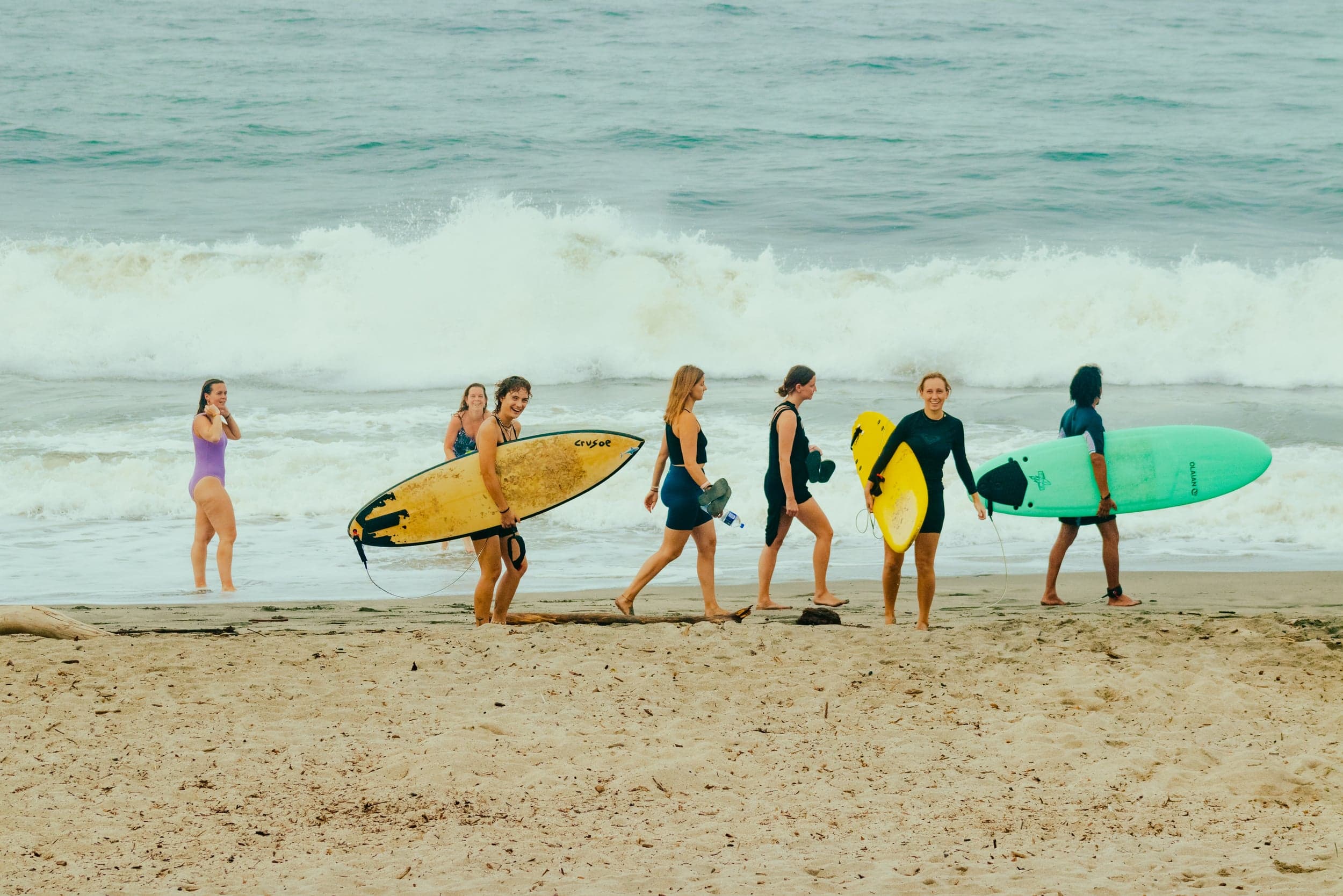 Group of women carrying surfboards along the wet sand after a session, waves breaking behind