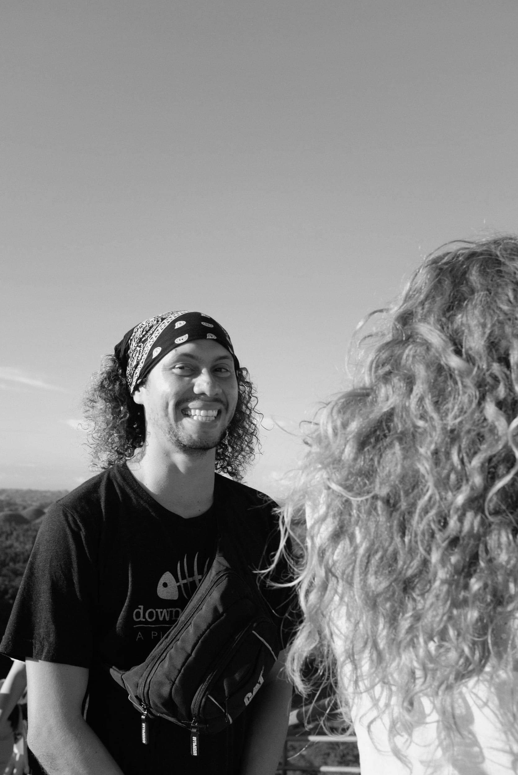 The photographer smiling in a bandana while chatting with a curly-haired woman outdoors