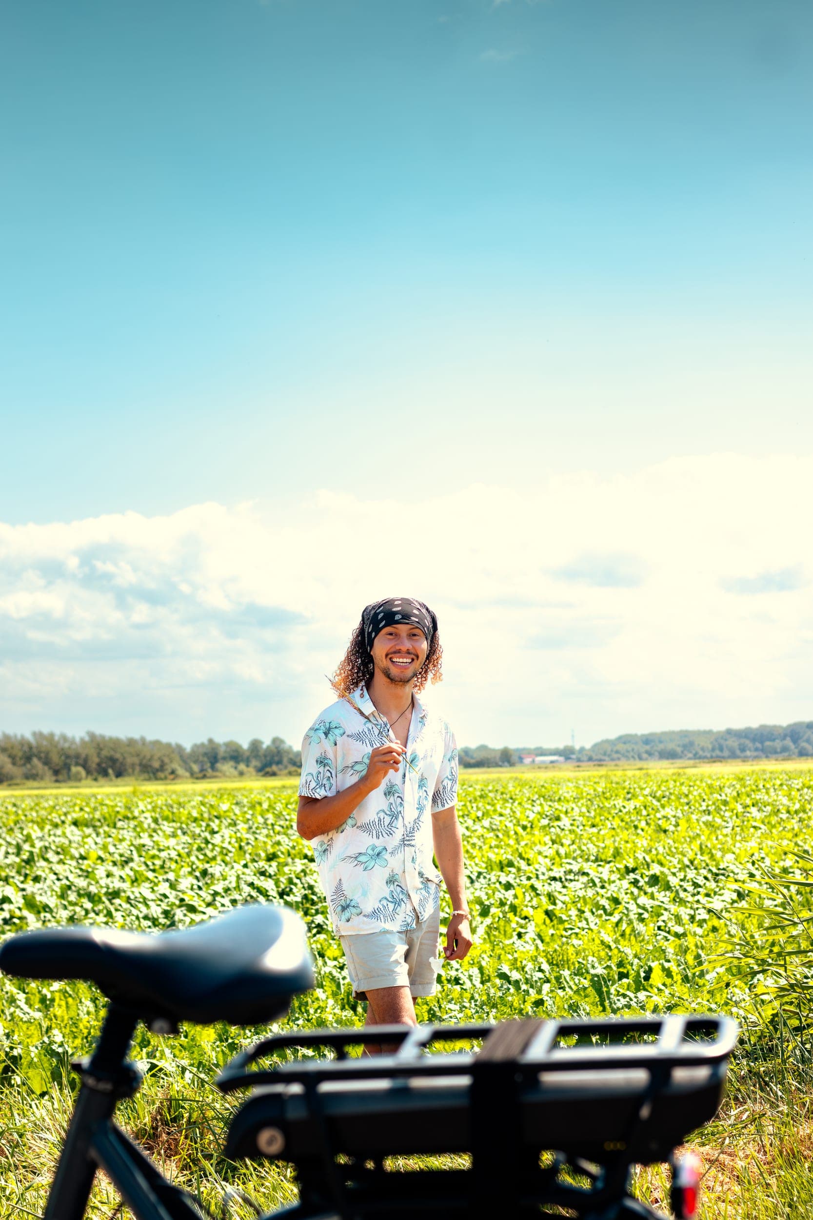 The photographer in a floral shirt standing in a green field beside a bicycle