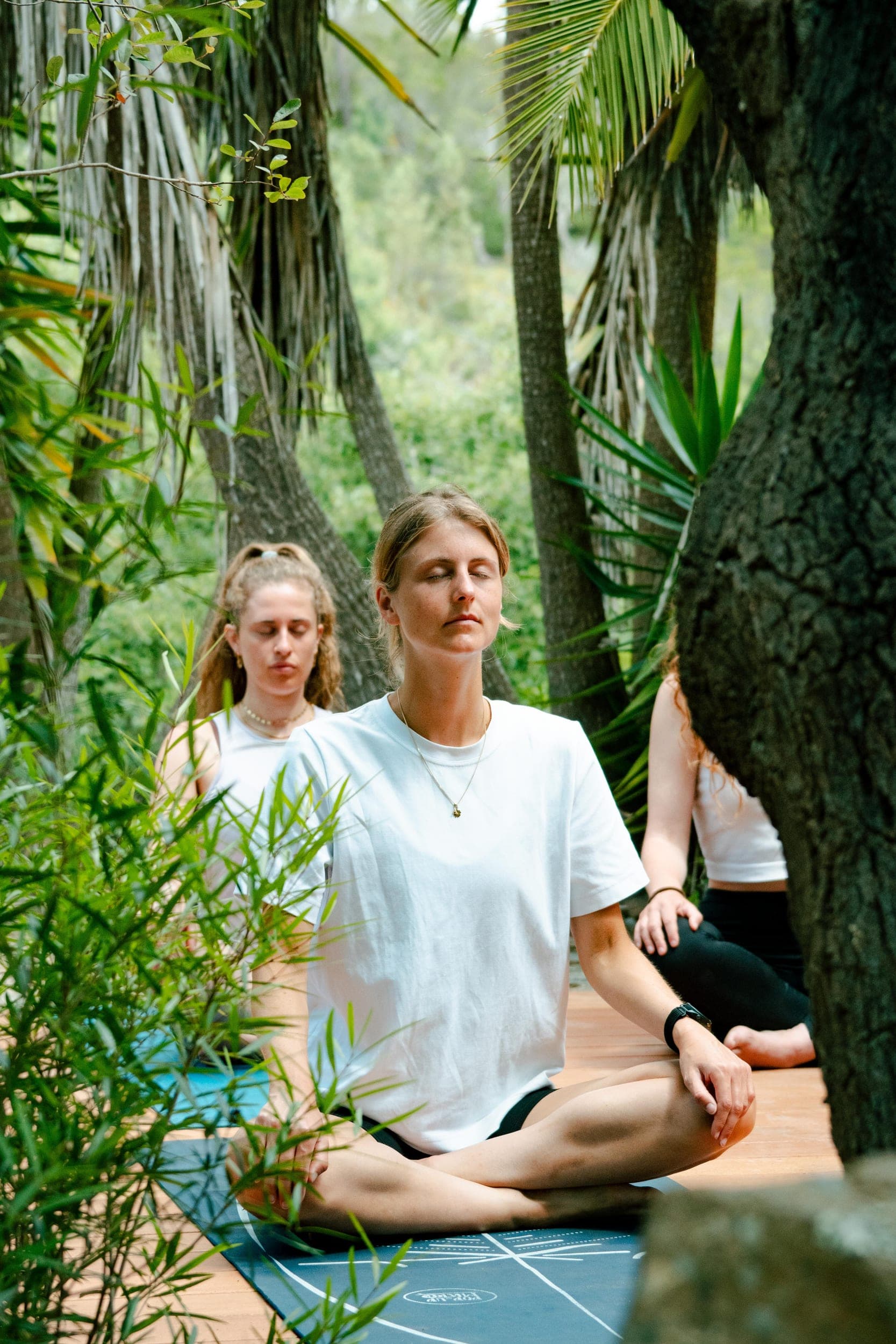 Woman meditating cross-legged with eyes closed among palm trees and greenery