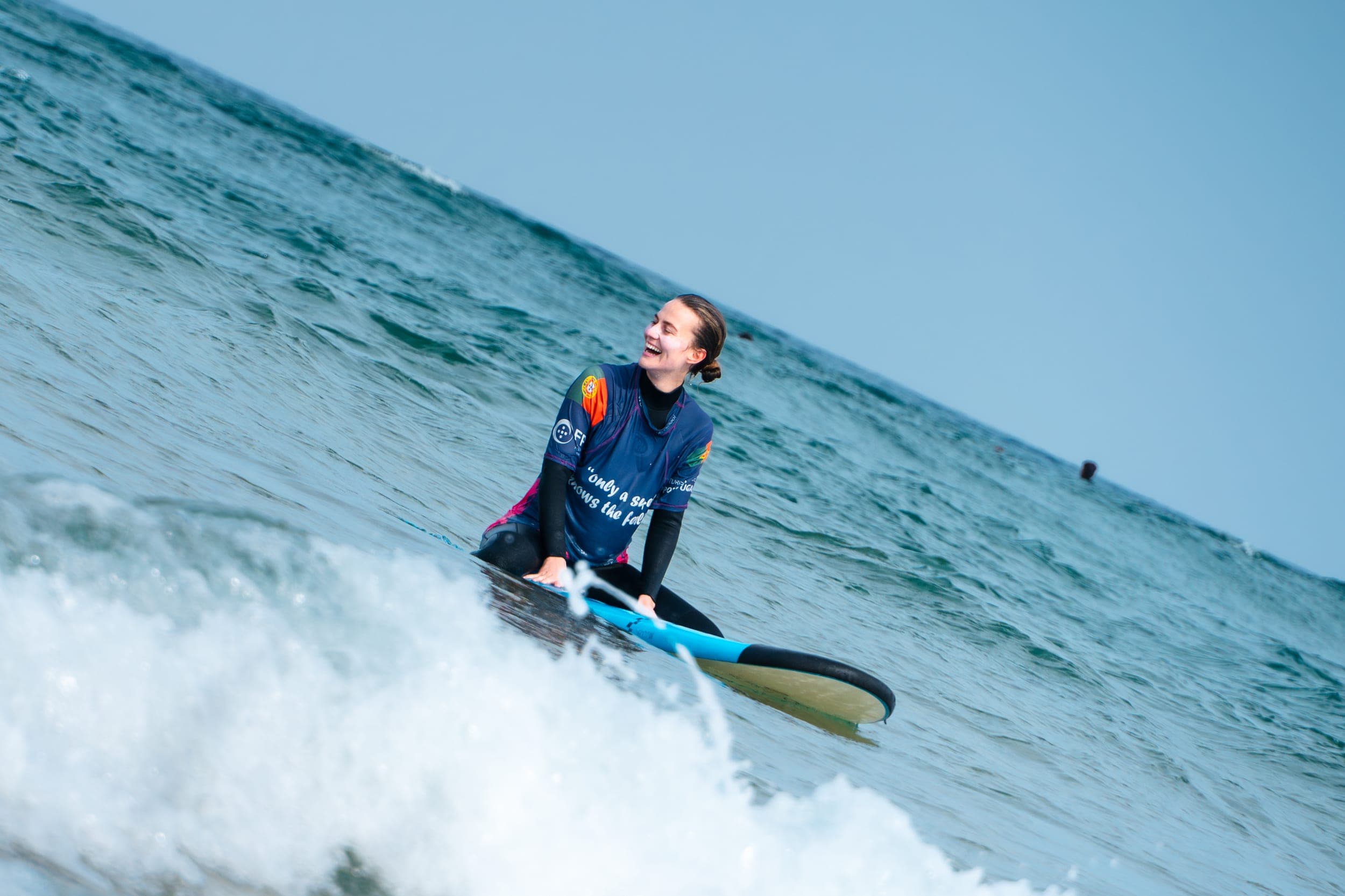 Laughing woman kneeling on her blue surfboard while riding a small wave