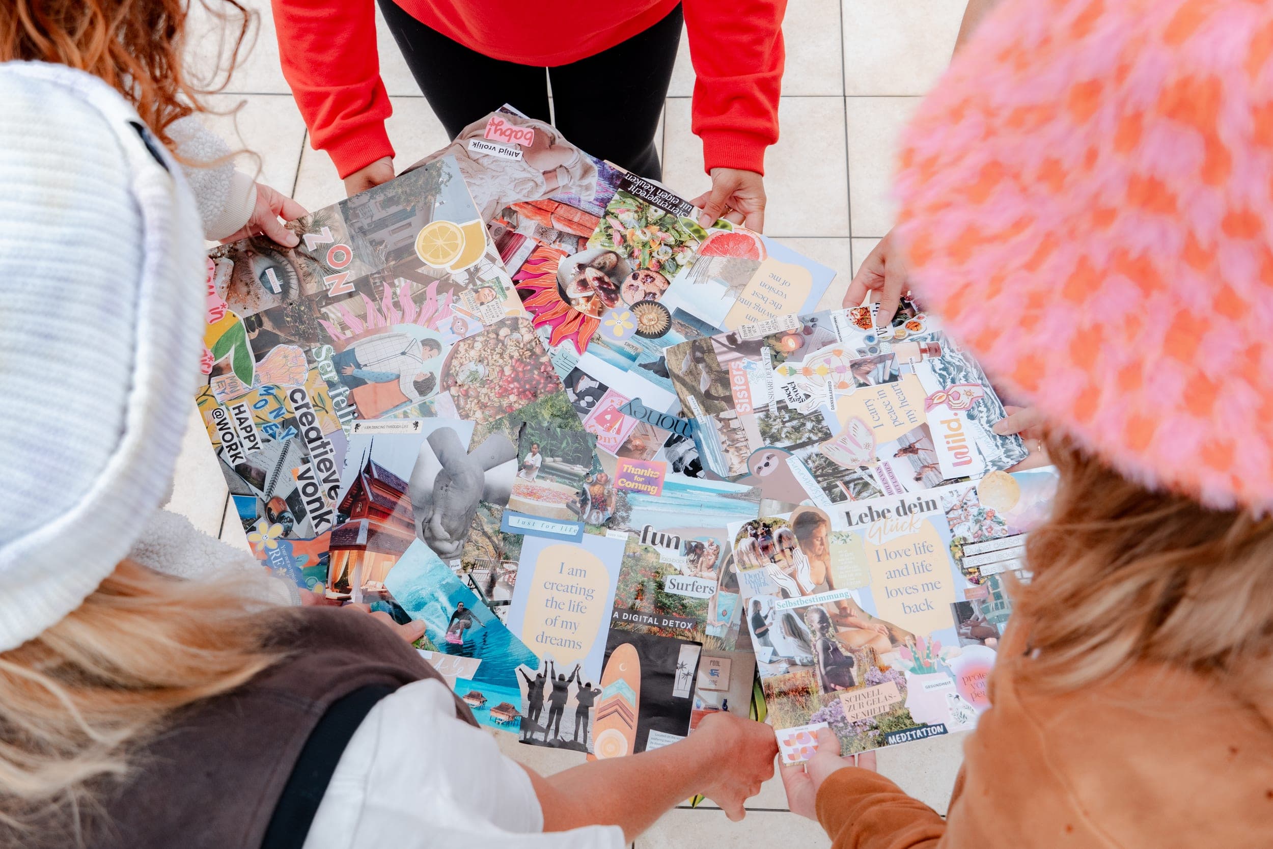 Overhead view of women holding colourful vision board collages on a tiled floor