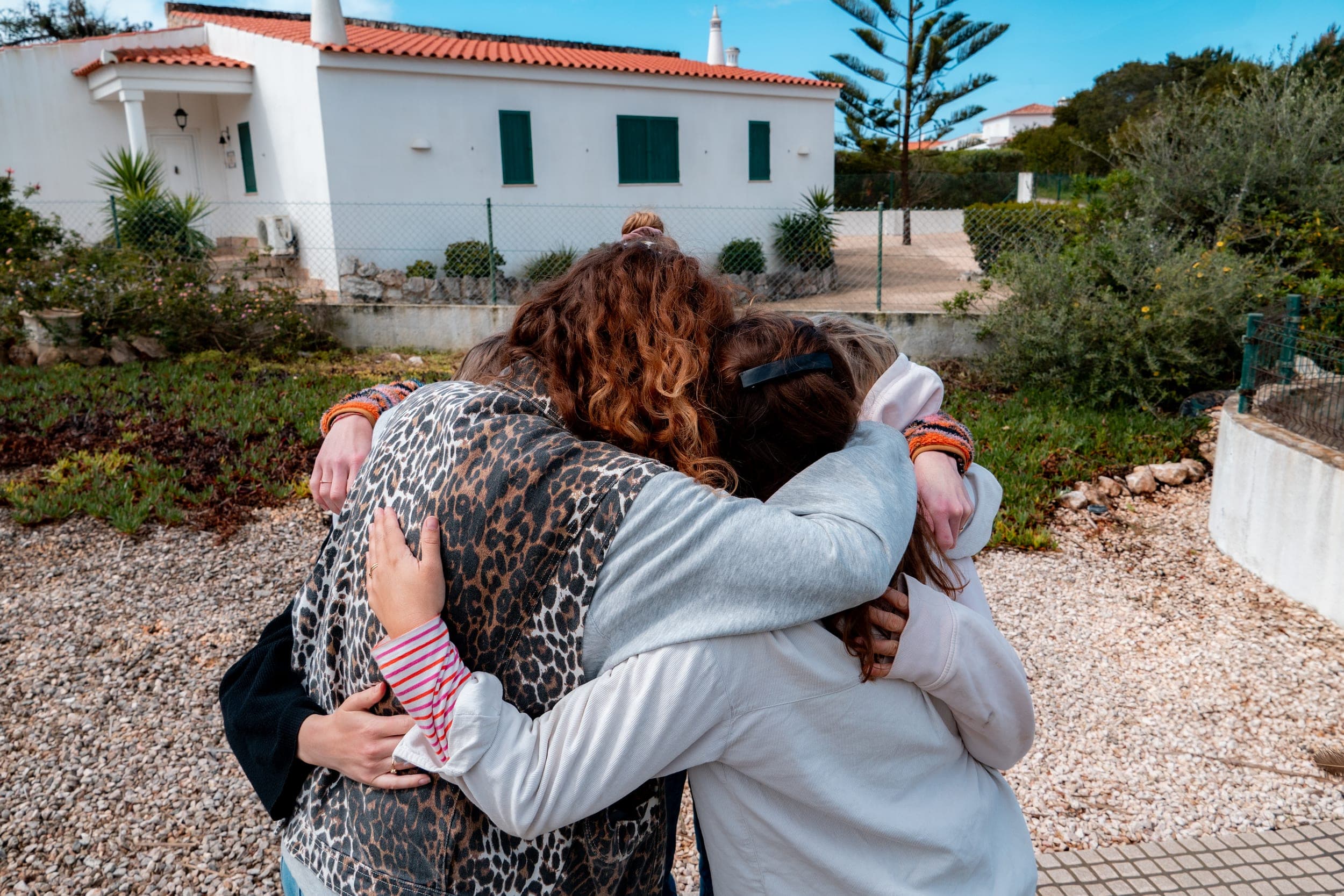 Three women embracing in a group hug facing a white Algarve villa with red roof