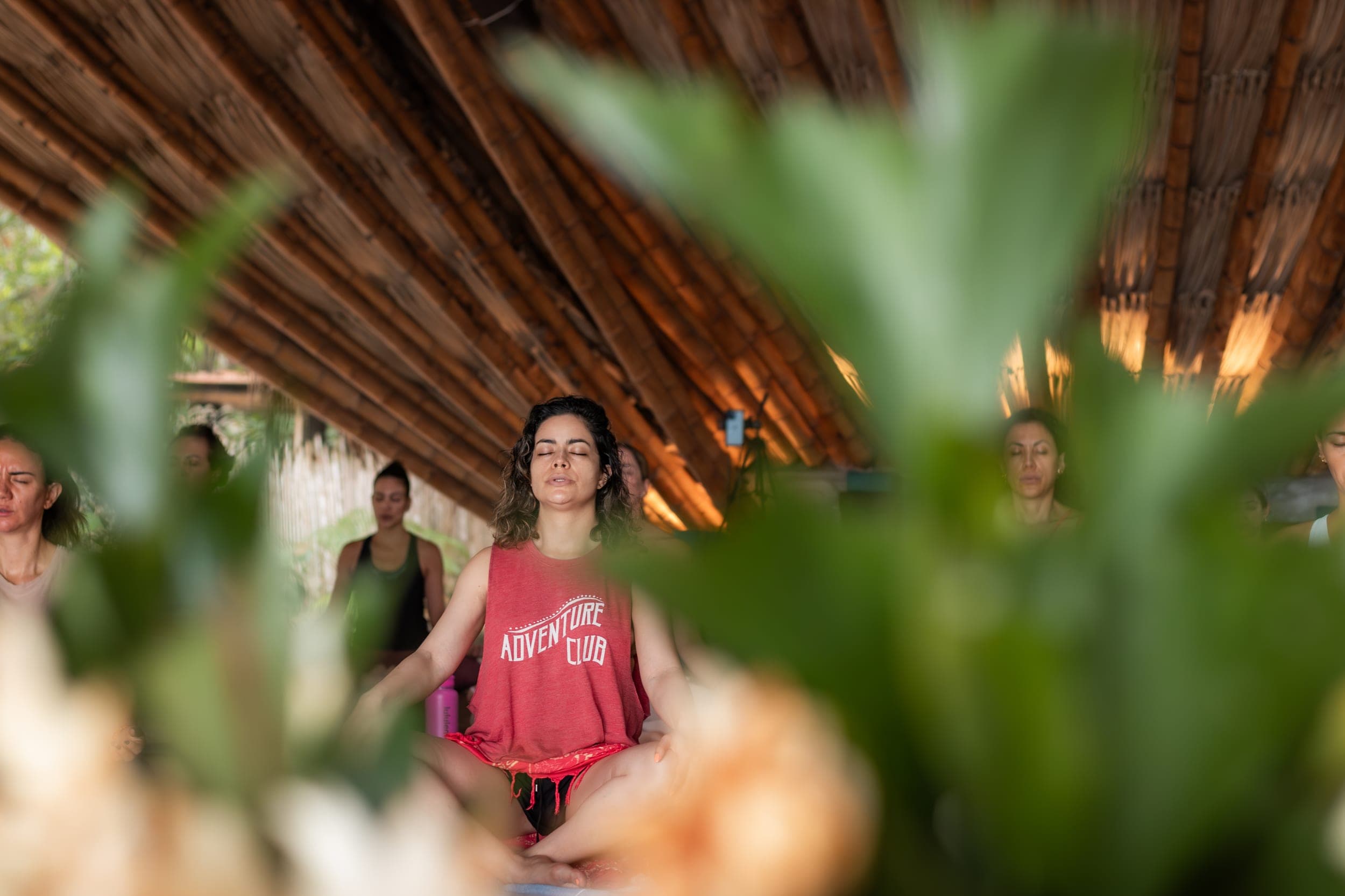 Woman meditating cross-legged under a bamboo roof, framed by tropical foliage