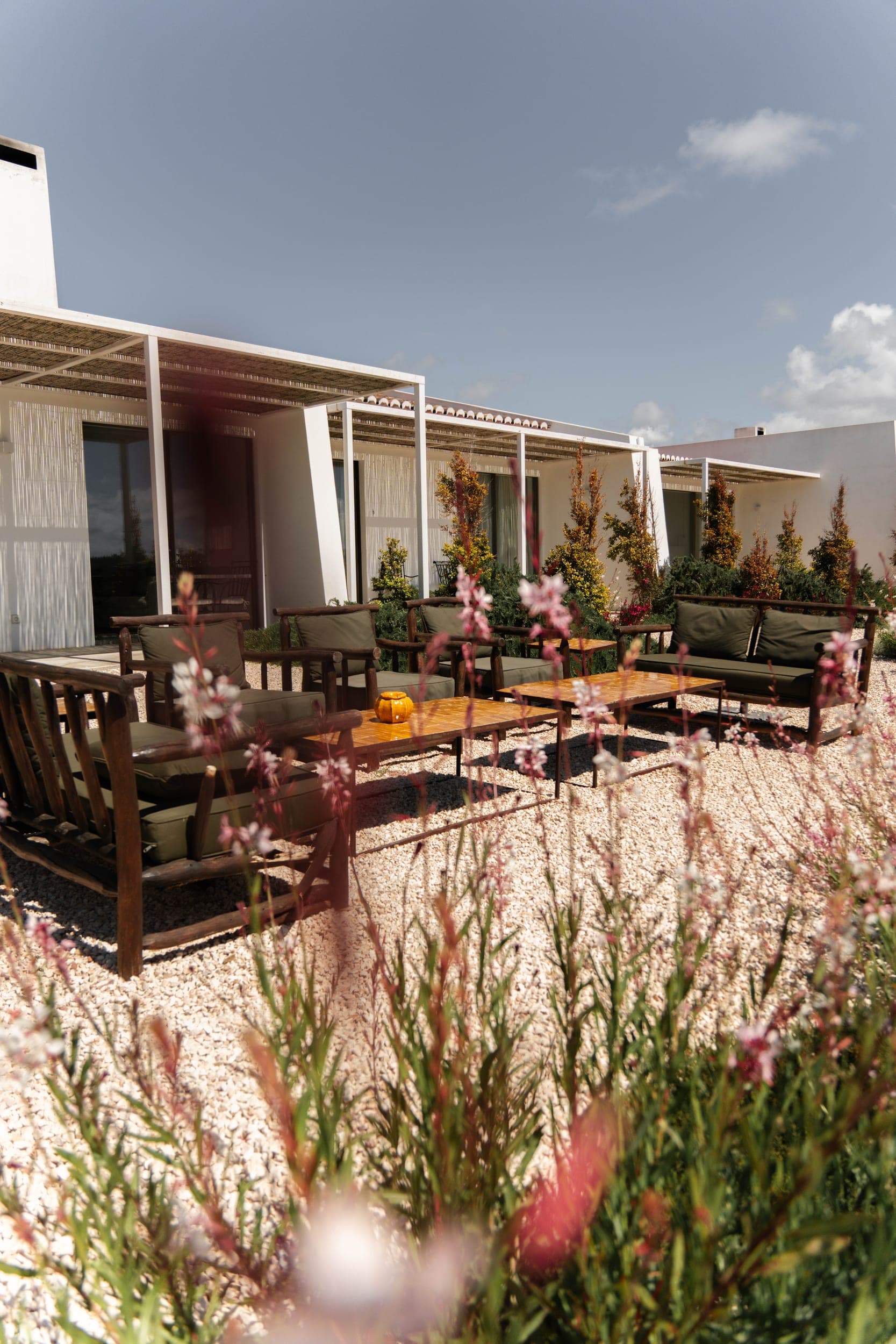 White villas with pergolas and rustic green armchairs on a gravel courtyard among wildflowers