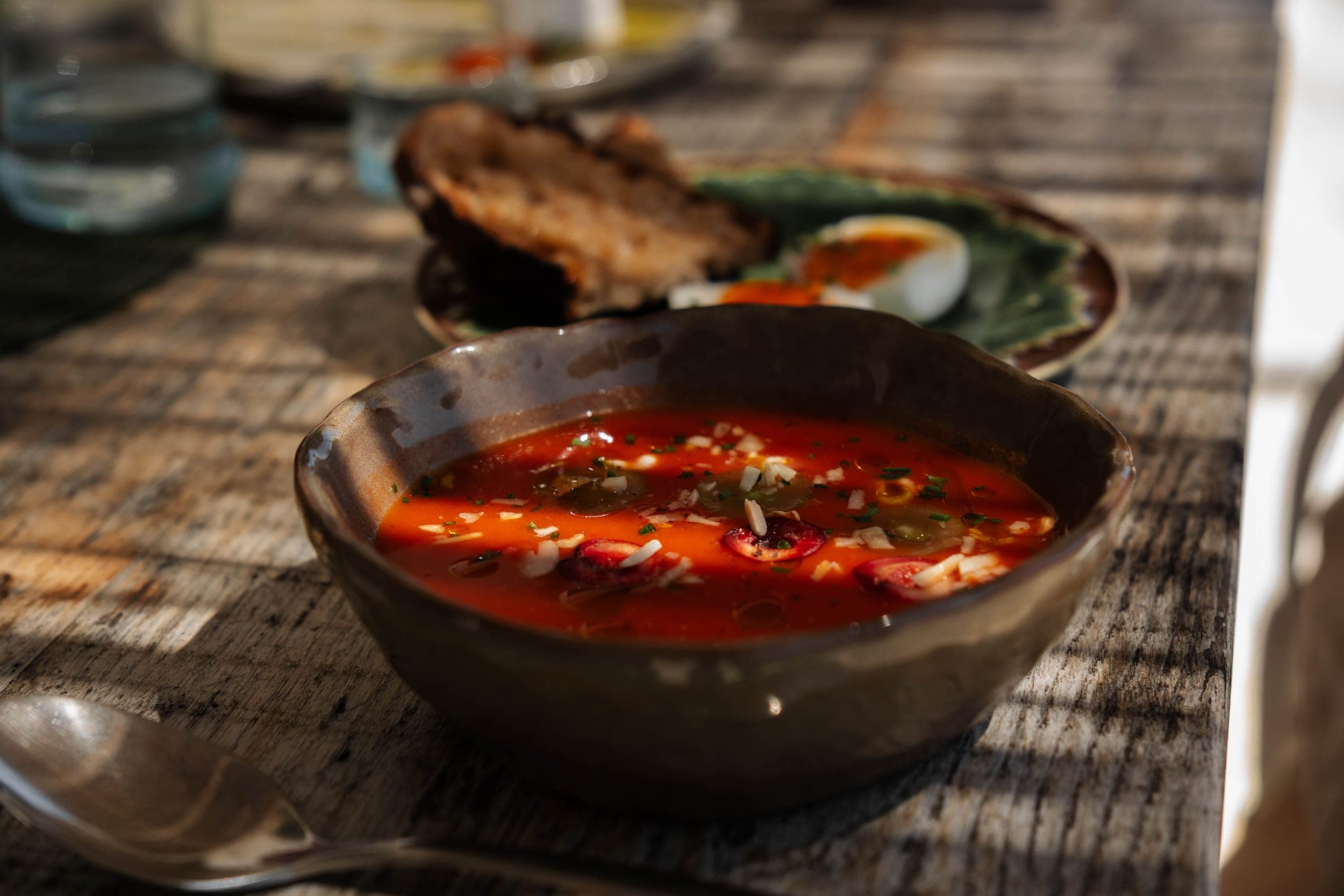 Bowl of chilled tomato gazpacho garnished with cherries and herbs on a rustic wooden table
