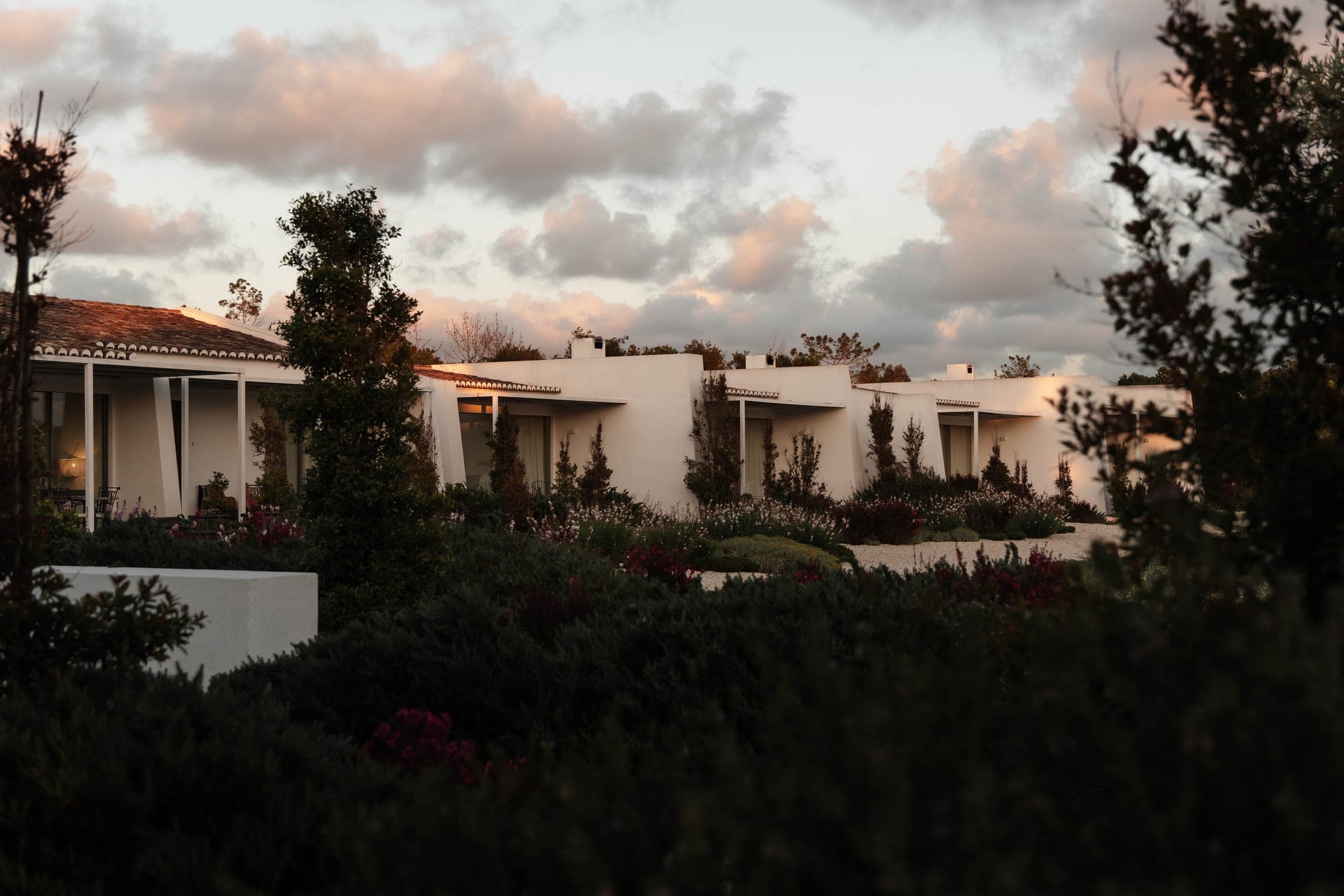 Row of white villas at dusk framed by cypress trees and flowering shrubs