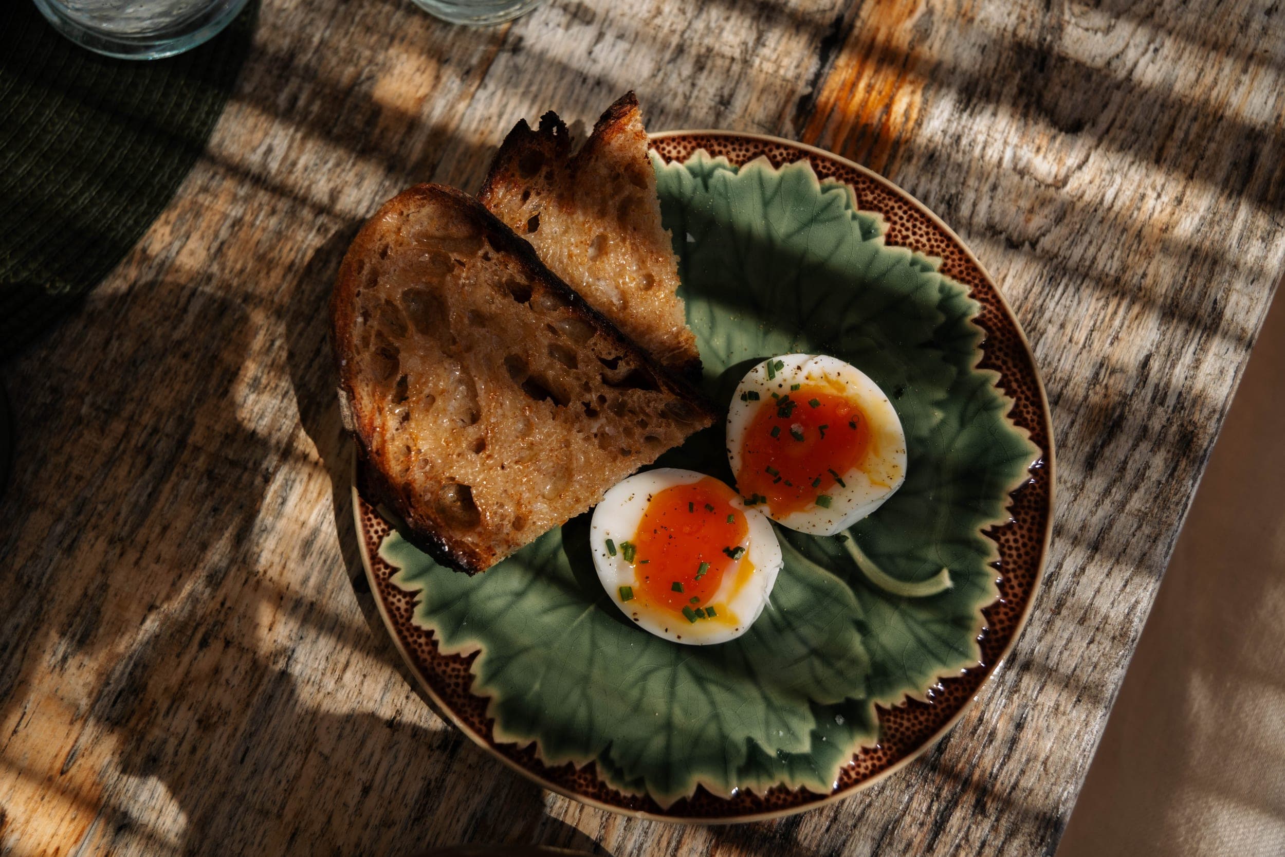 Runny soft-boiled eggs with chives and grilled sourdough on a green leaf-shaped plate