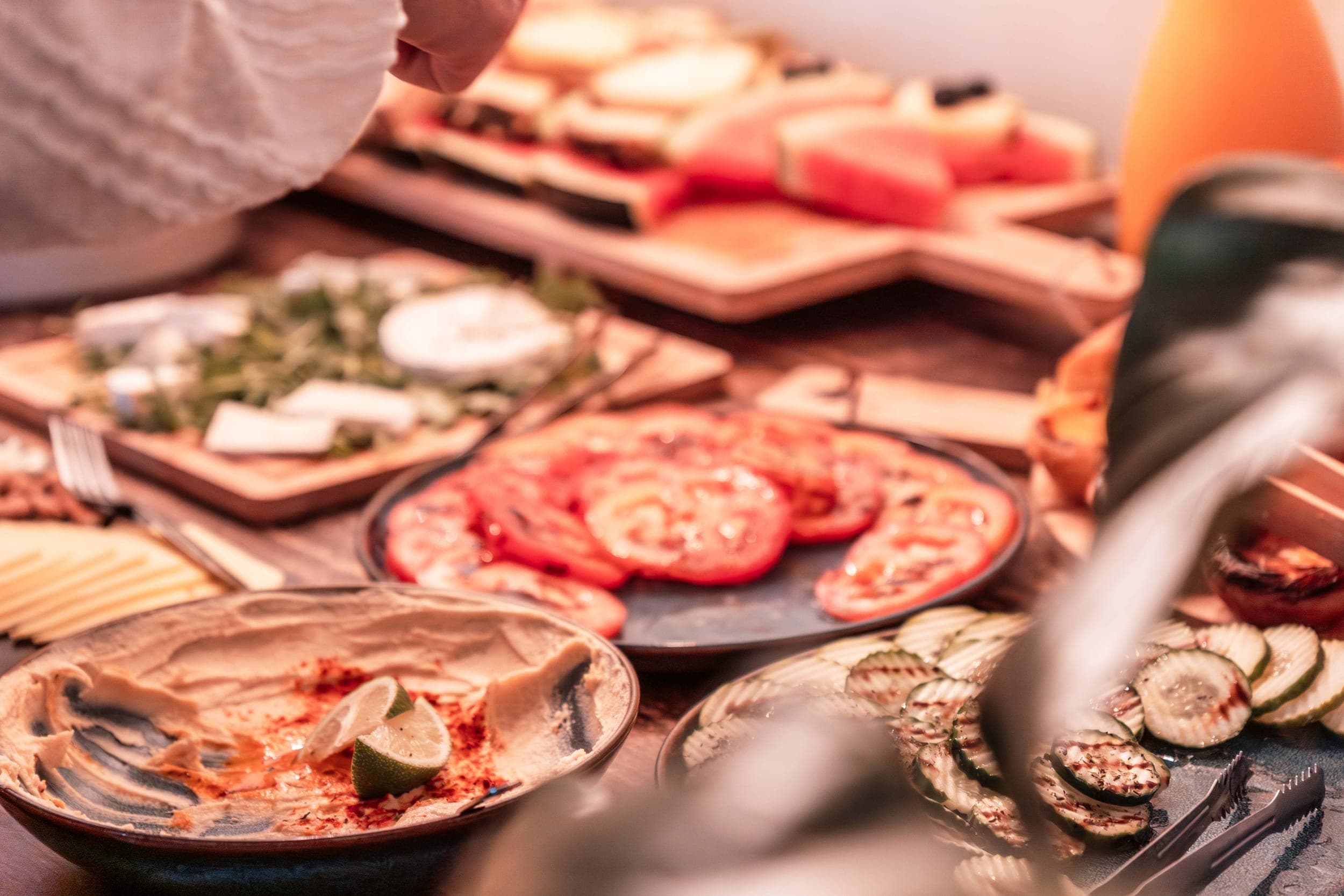 Buffet spread of sliced tomatoes, hummus, grilled cucumber and cheese on a wooden table