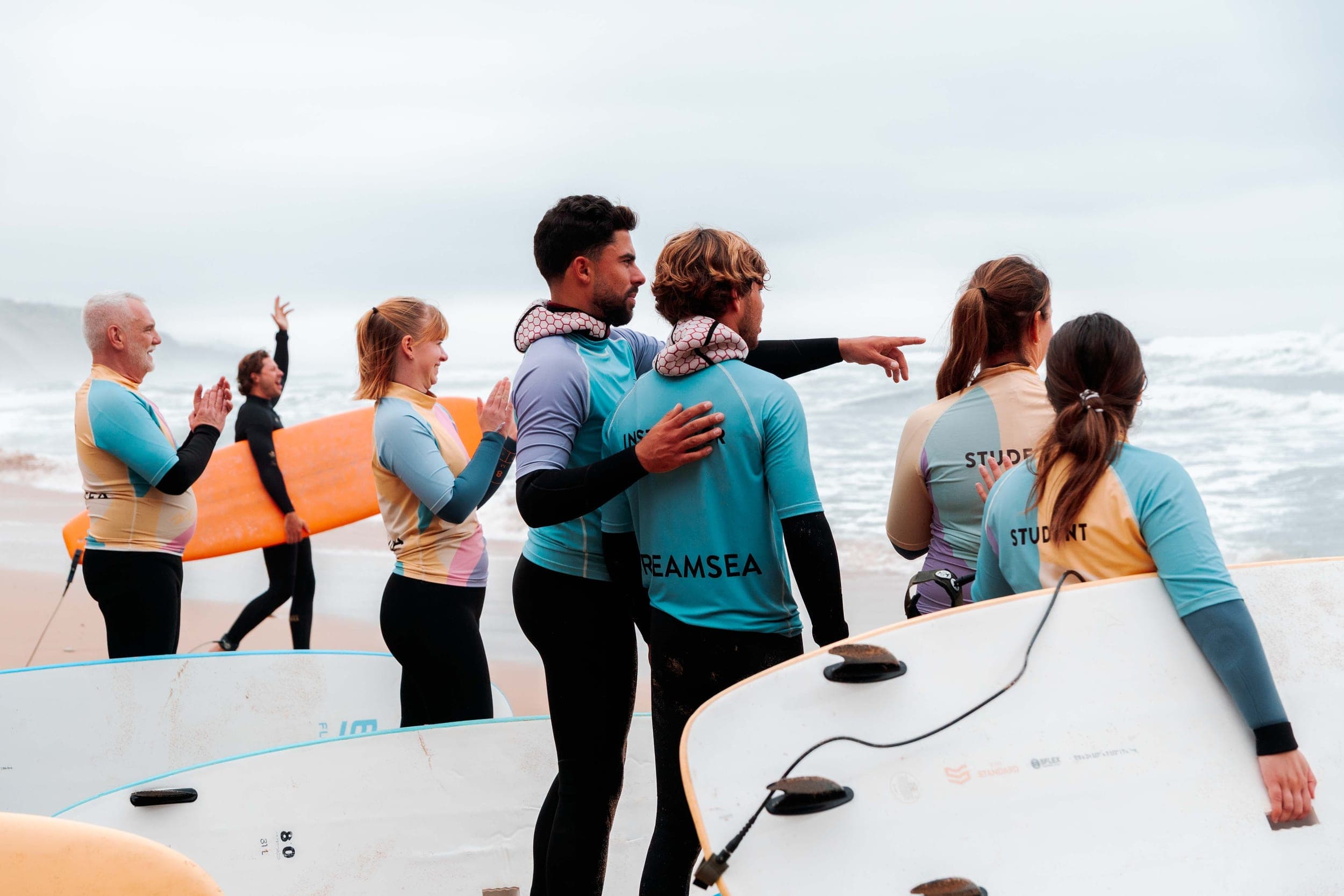 Surf group in rash vests hugging and cheering together on an overcast beach