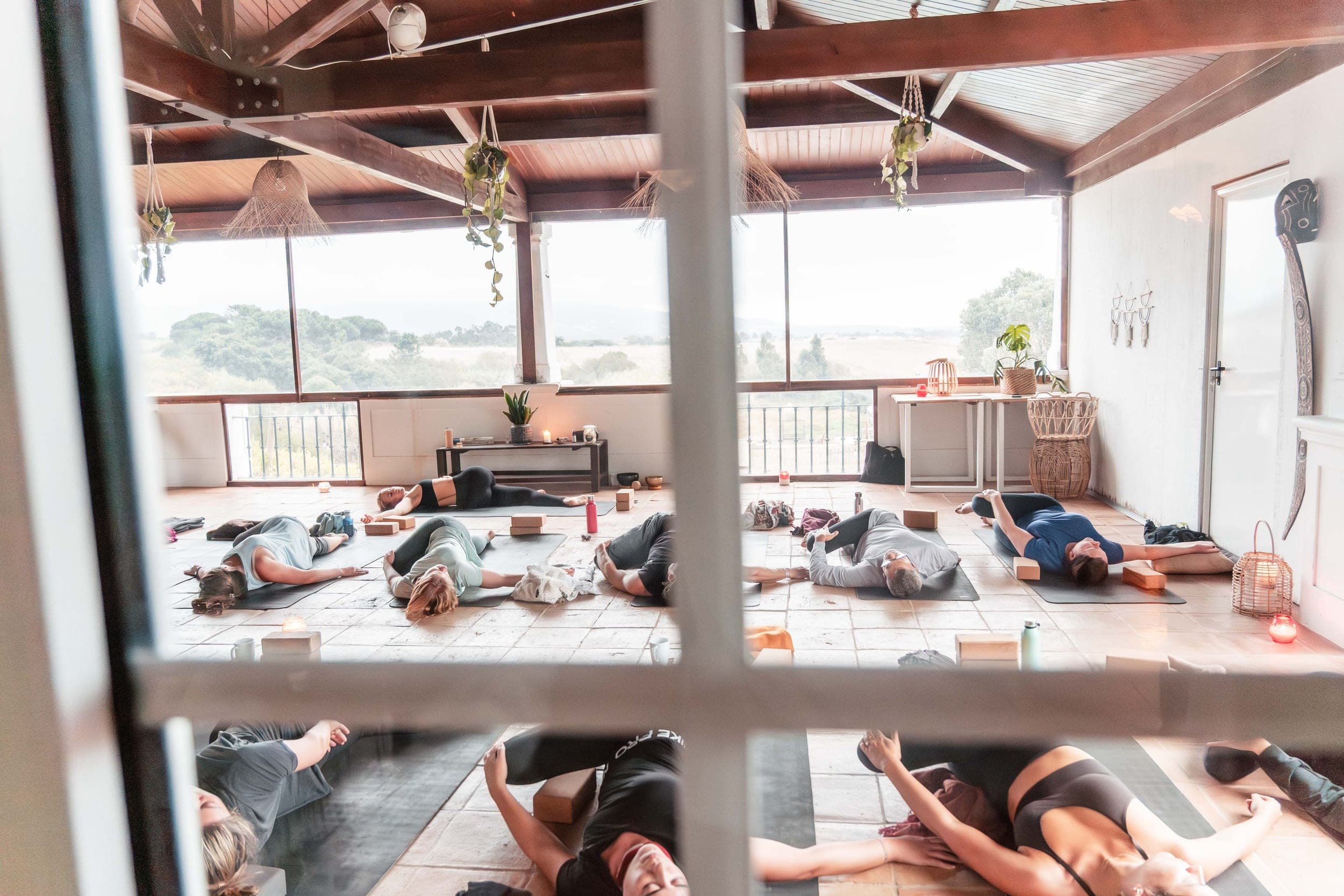 Group lying in relaxation pose on yoga mats in an airy studio with countryside views