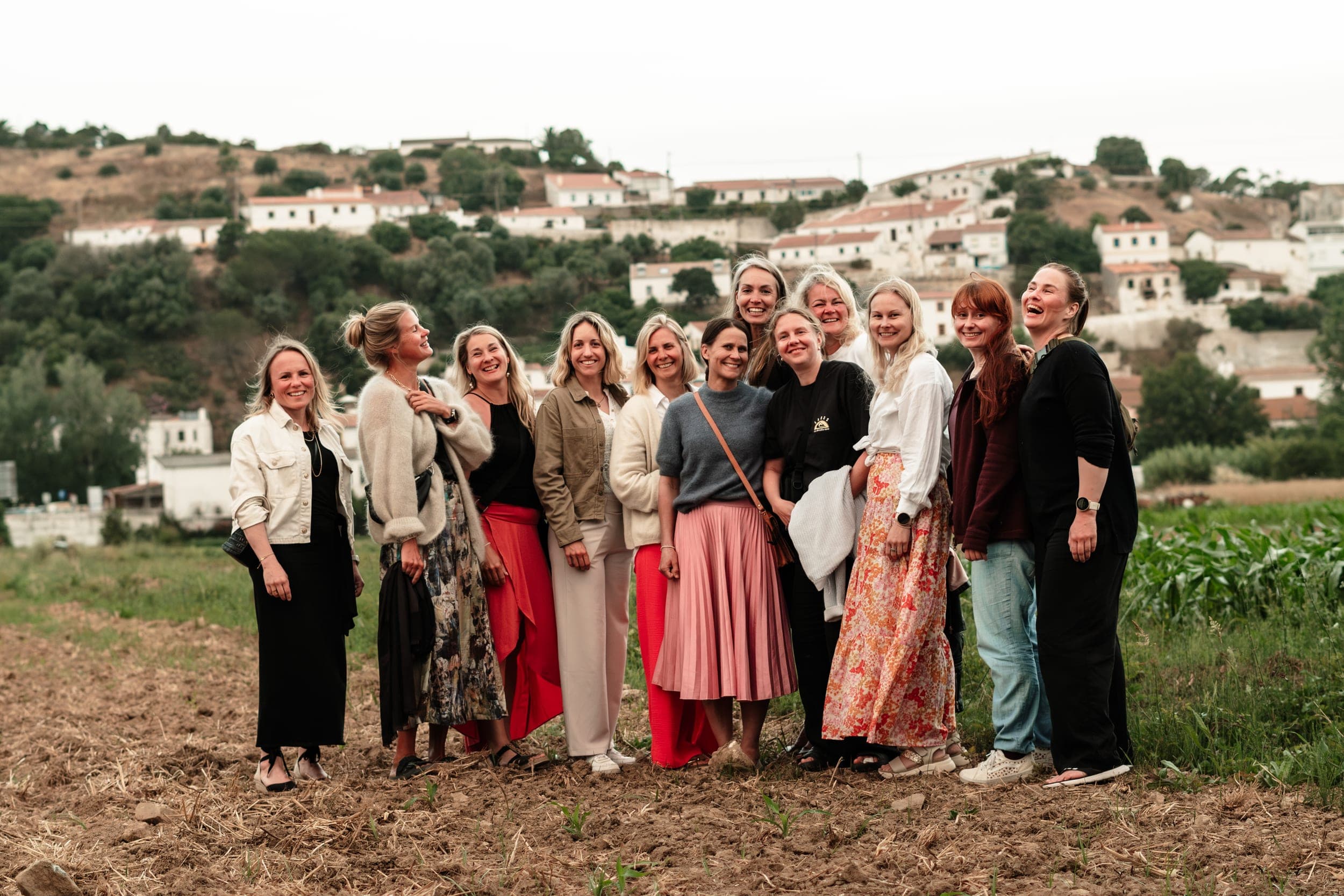 Large group of women laughing together in a field below a whitewashed Portuguese hilltop village
