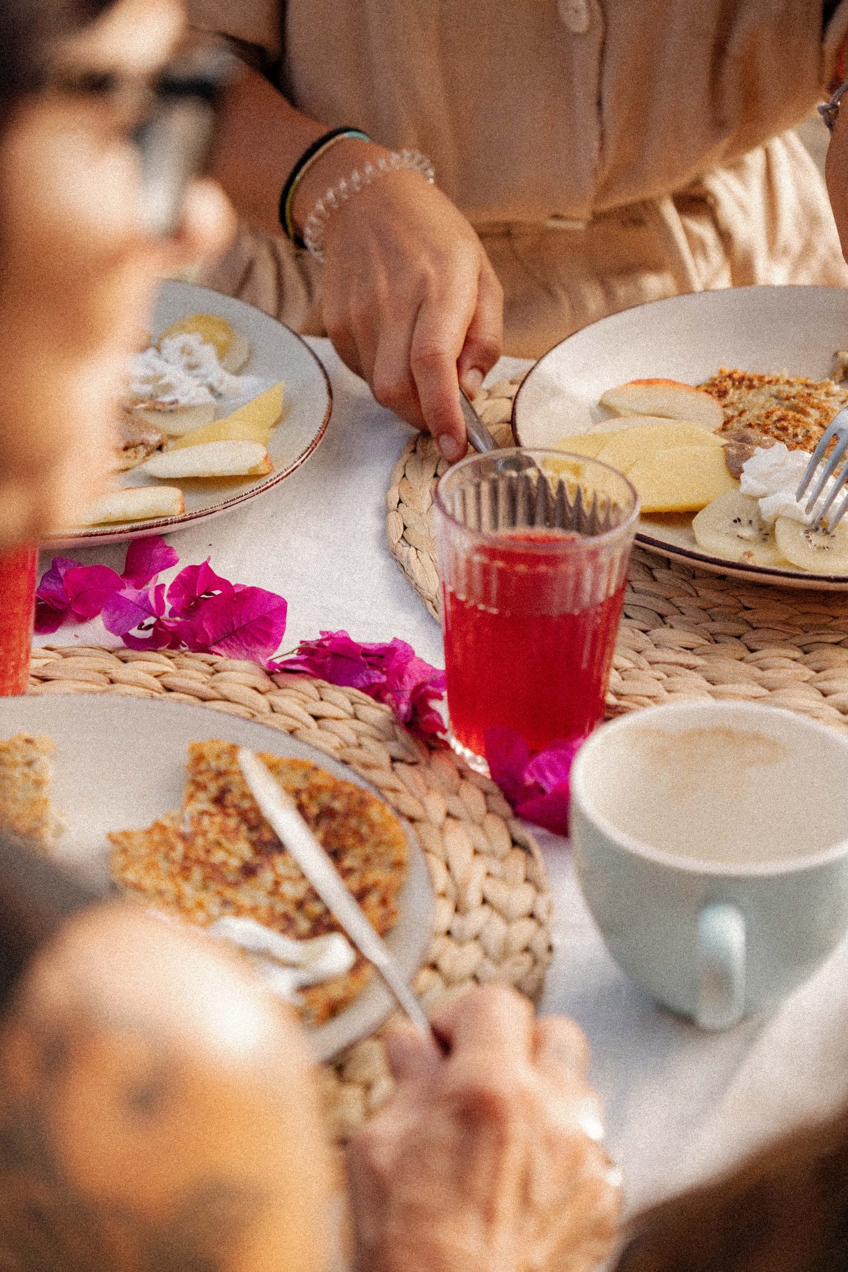 Women eating a healthy breakfast of pancakes and fruit with pink juice and bougainvillea petals