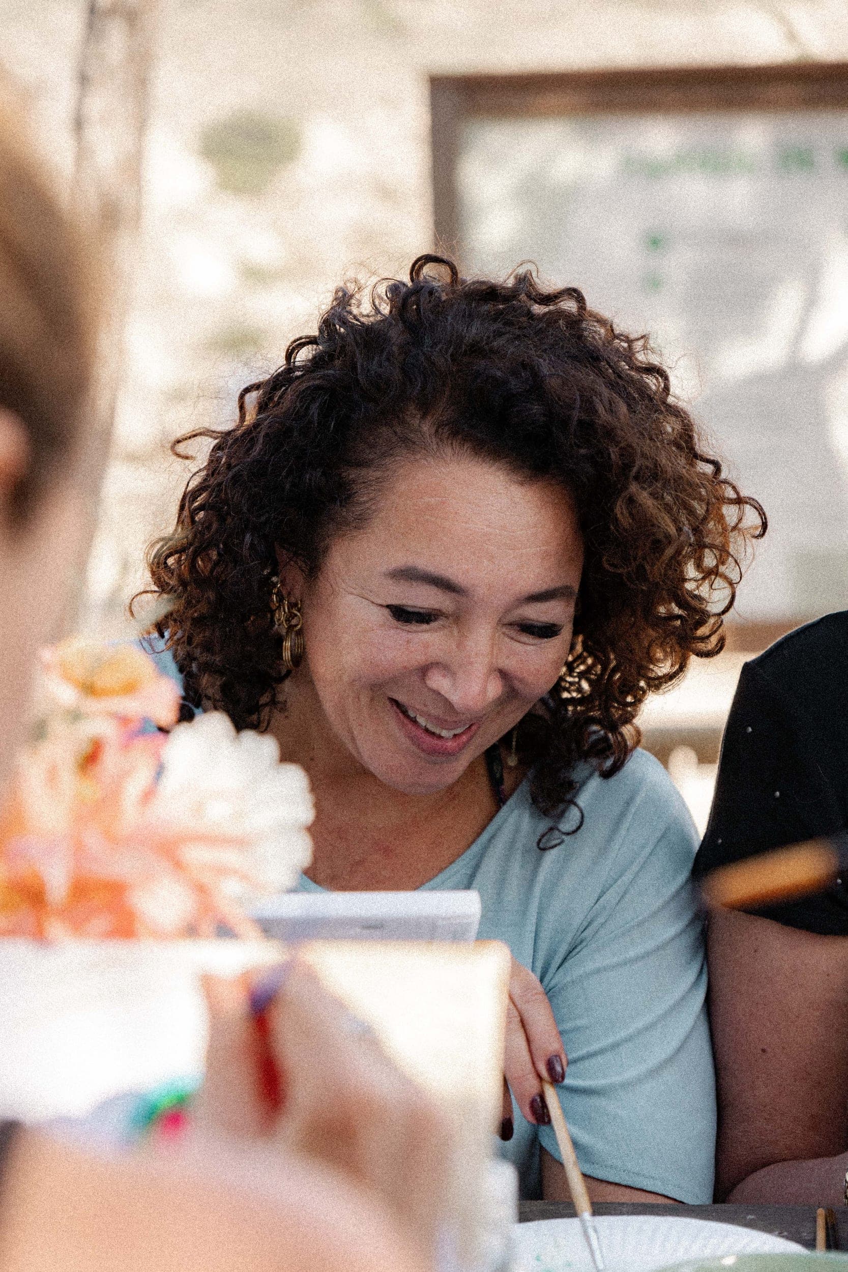 Smiling curly-haired woman painting with a brush during a creative wellness workshop