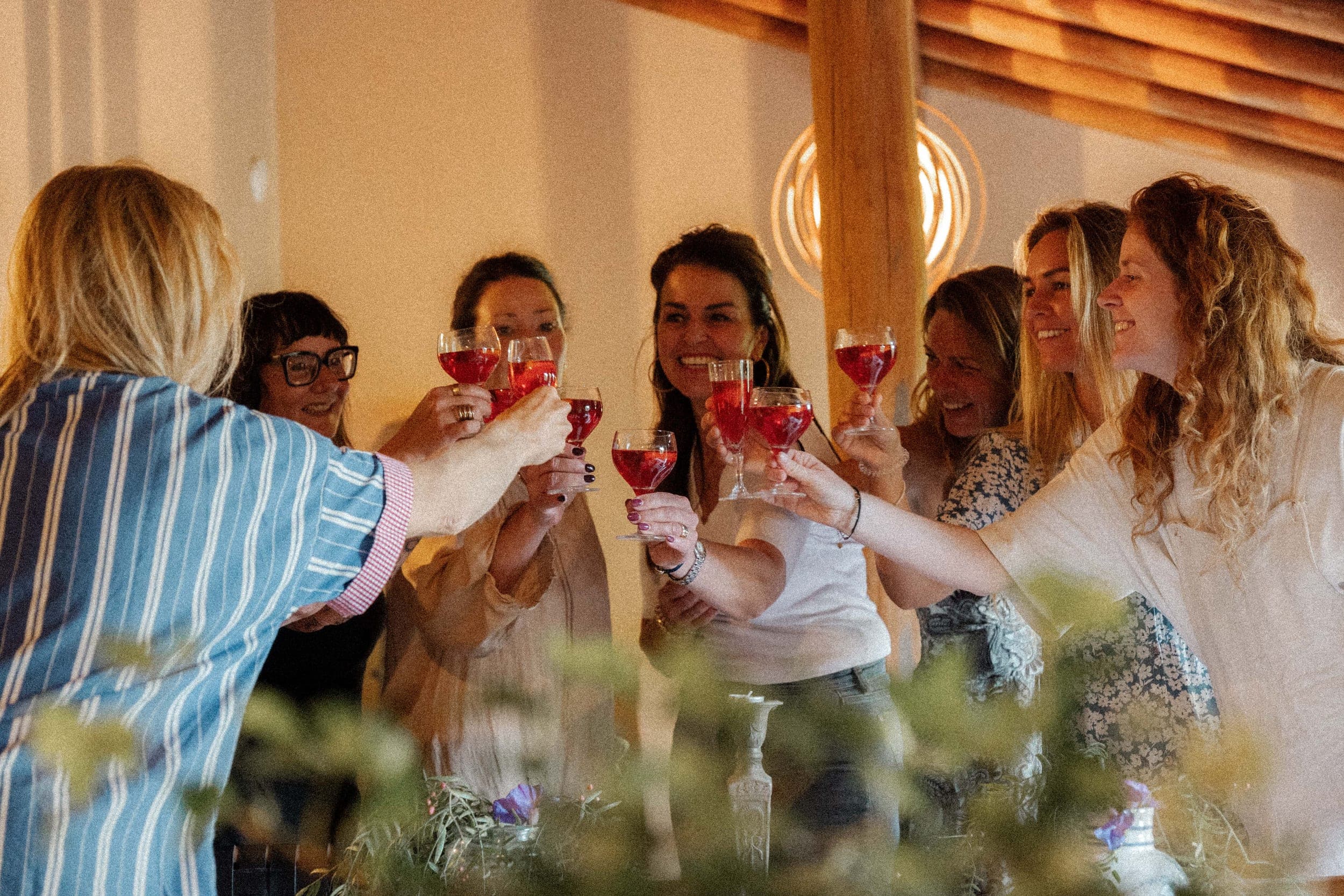 Women laughing and raising glasses of red drinks in a warm toast indoors at a retreat