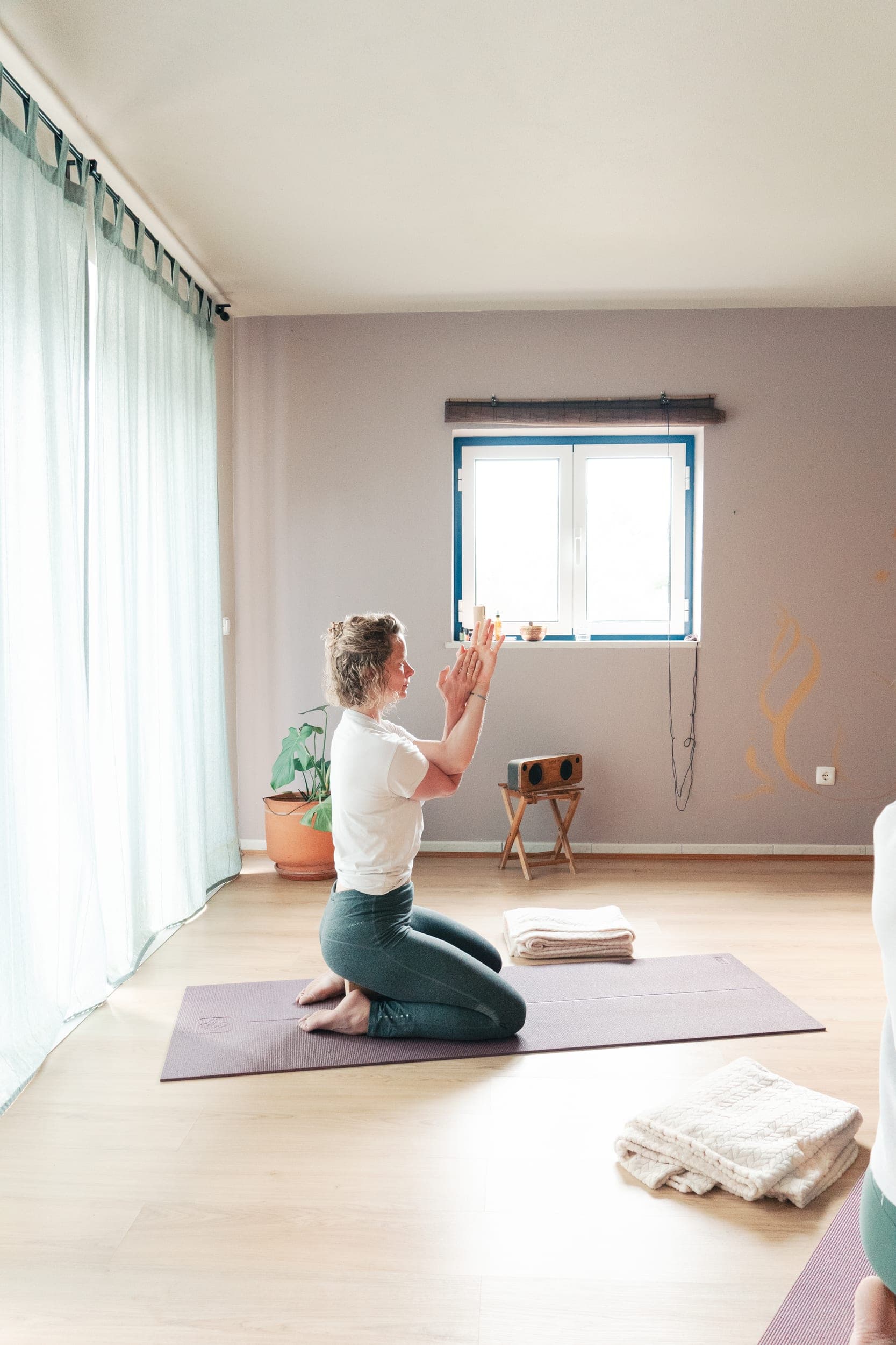 Woman kneeling in prayer pose on a mat in a serene sunlit yoga room