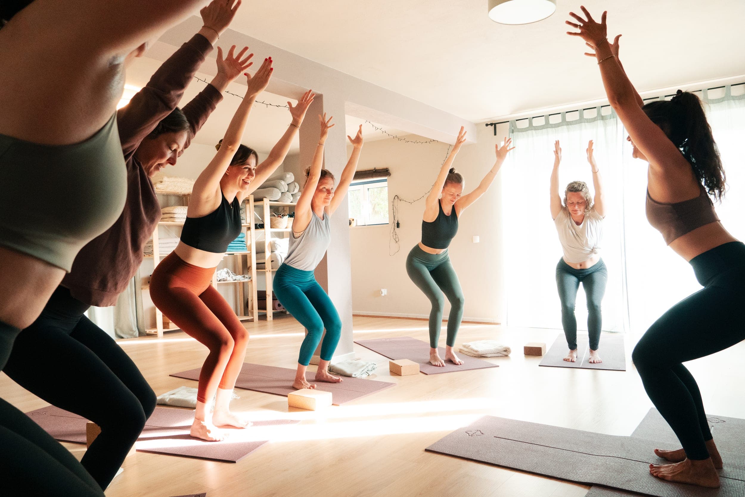 Women in chair pose with arms raised during a bright indoor yoga class